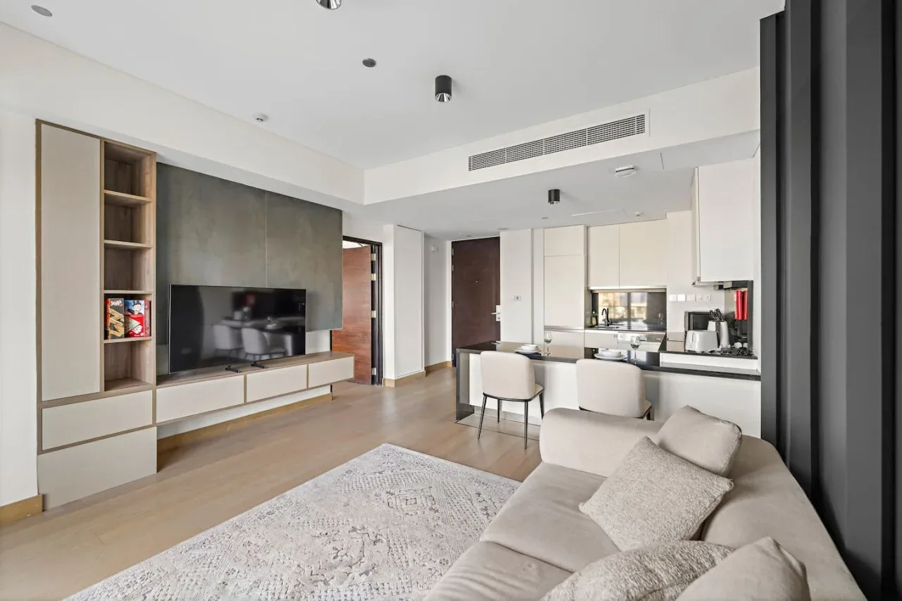 A modern living room with a television, seating, and an open kitchen.