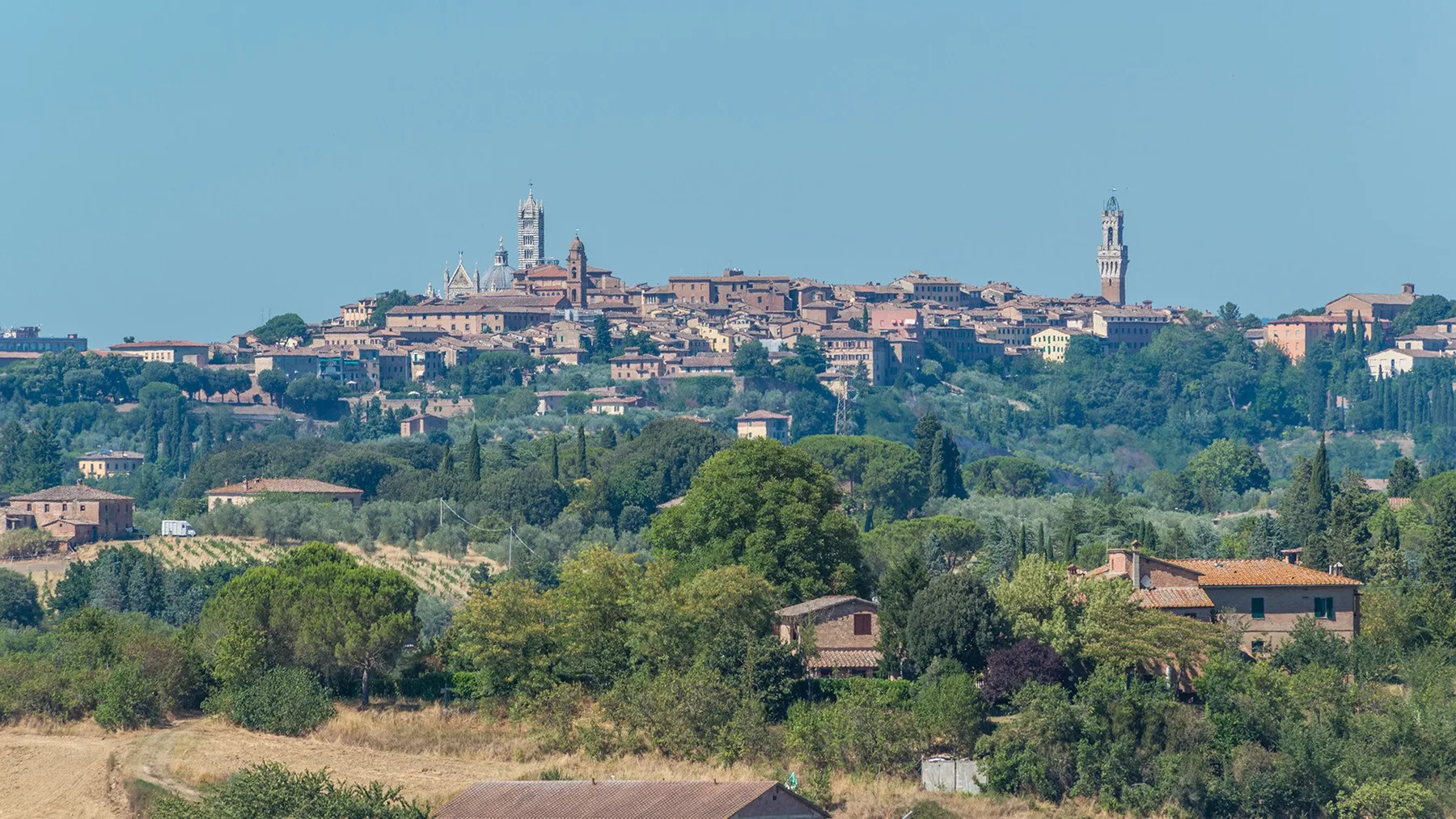 Un pueblo en lo alto de una colina se alza sobre un paisaje verde y arbolado.