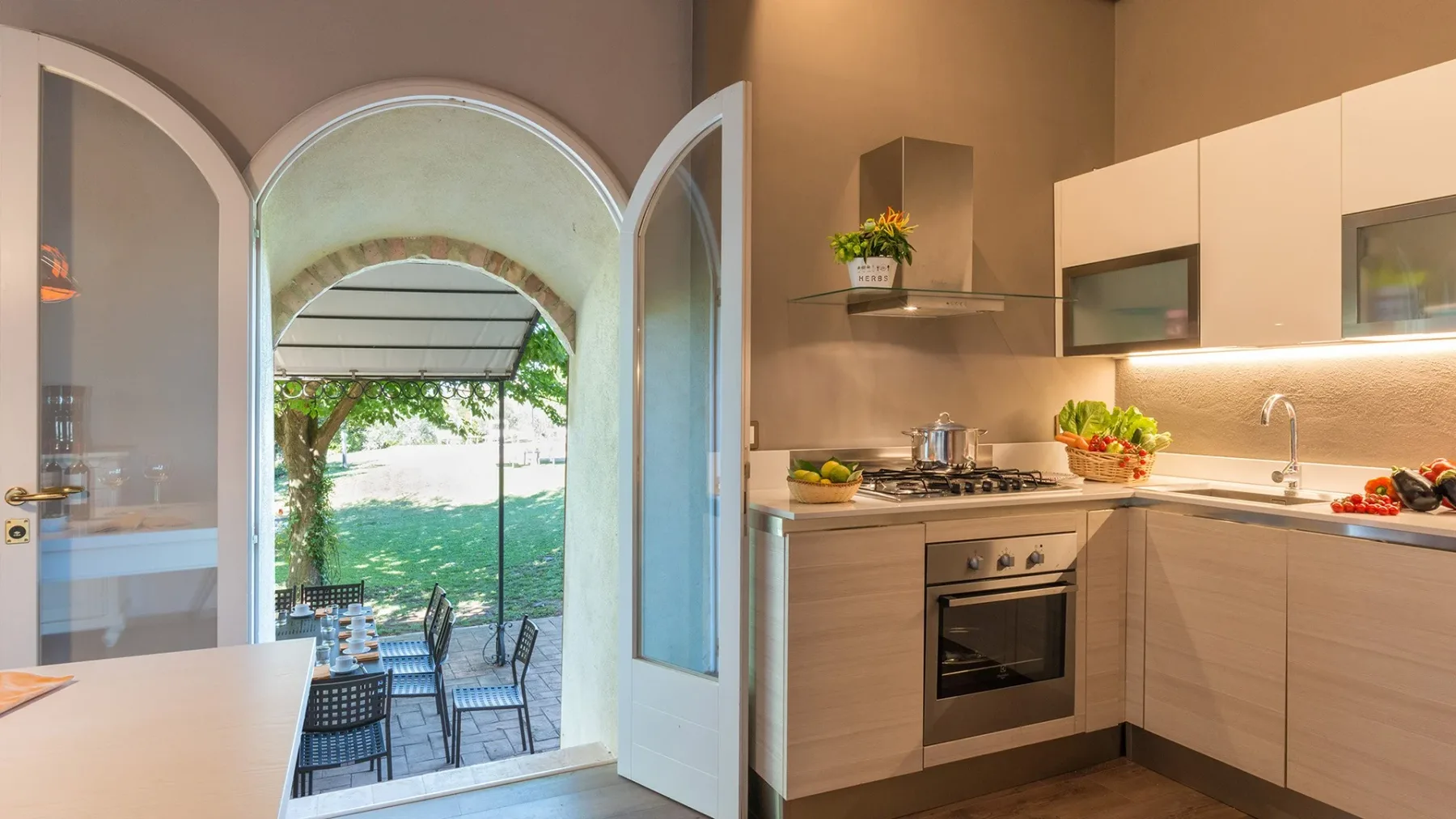 Una cocina moderna se abre, a través de puertas arqueadas, a un patio con asientos al aire libre.