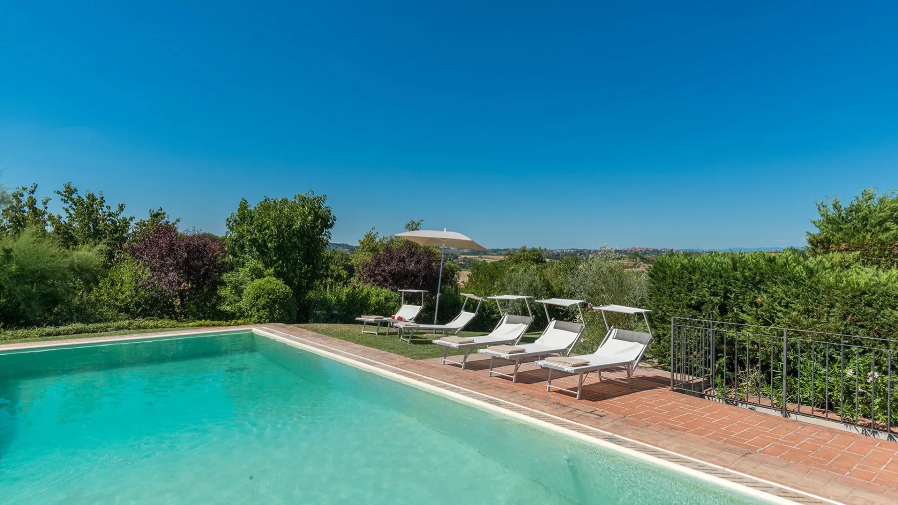 Una piscina exterior está junto a una terraza de baldosas y asientos reclinables.