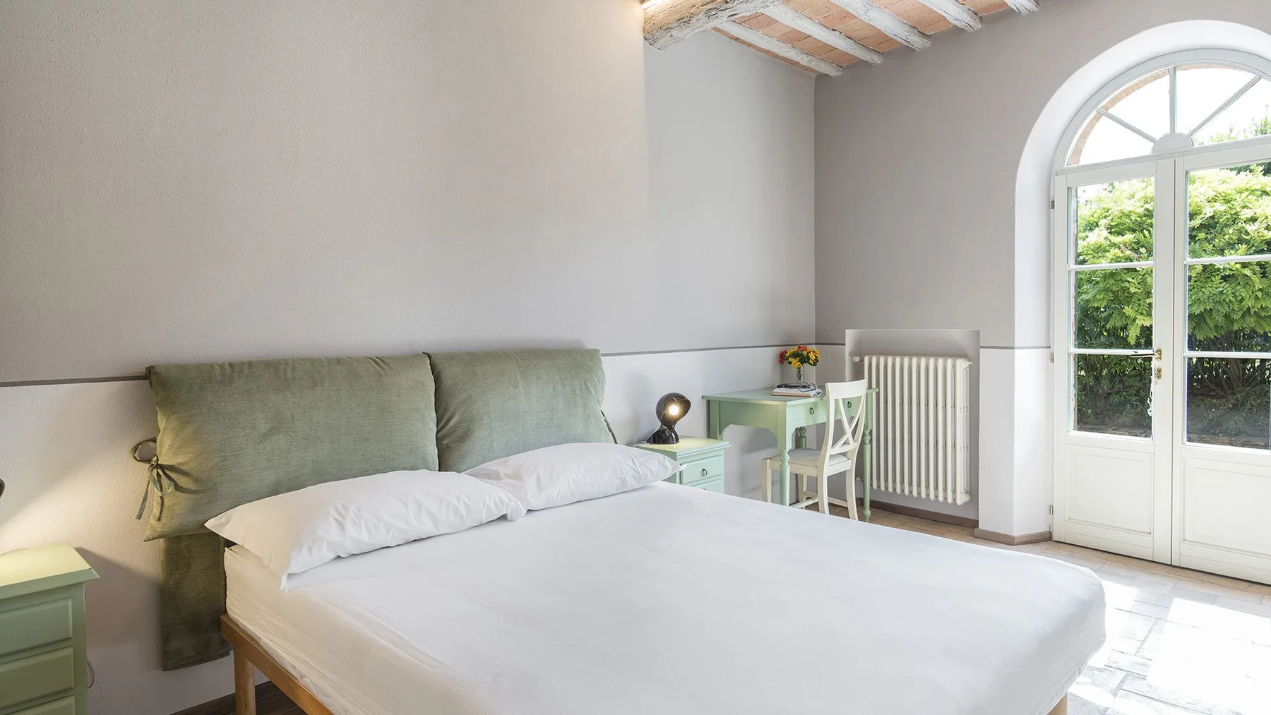 Un dormitorio luminoso con una cama junto a una puerta acristalada arqueada.