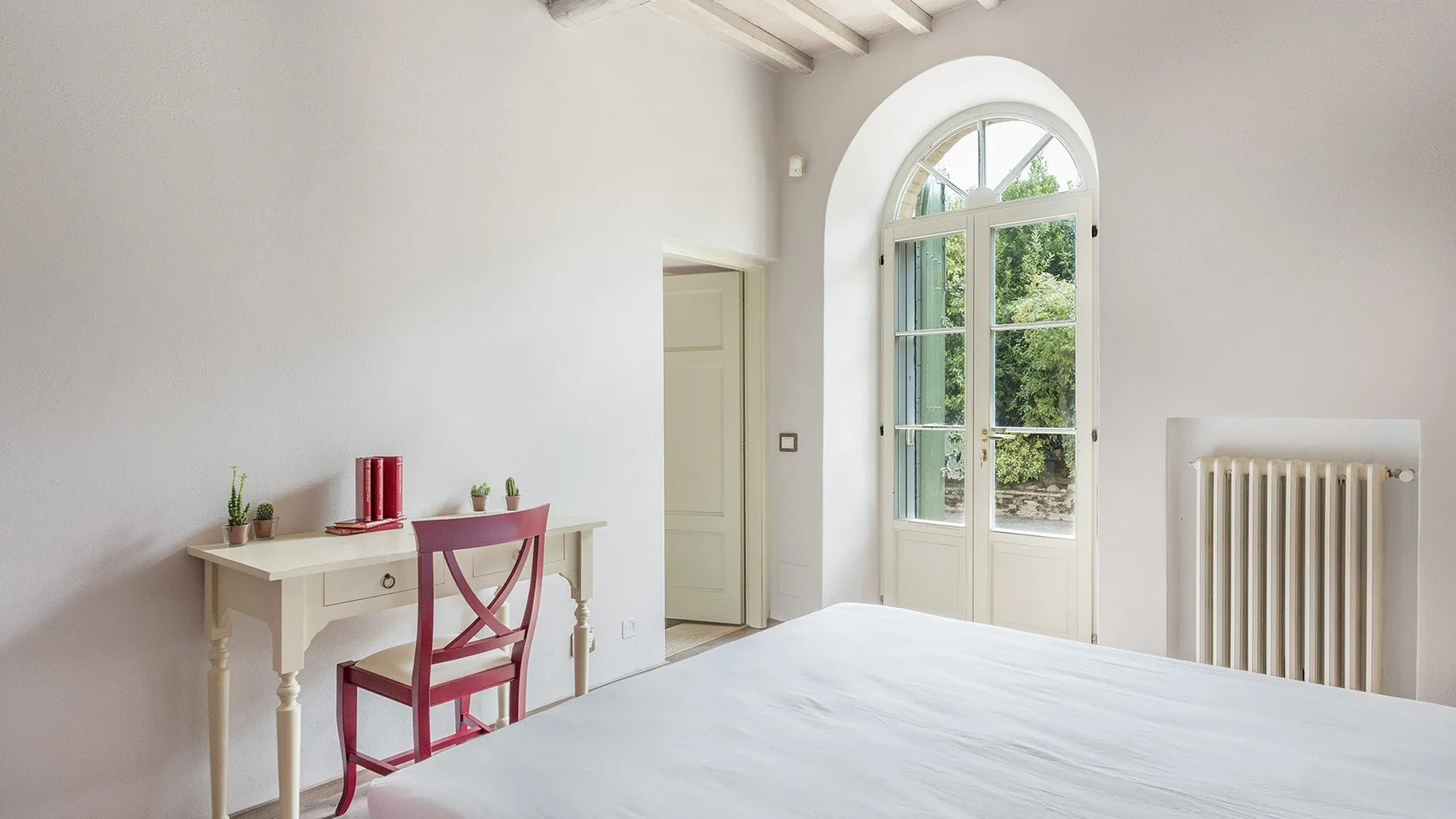 Un dormitorio luminoso con un escritorio junto a una ventana alta en arco.