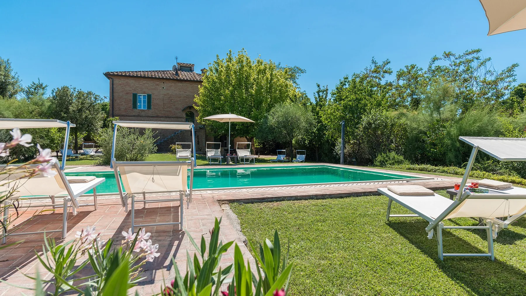 Una piscina al aire libre junto a un césped, con asientos y una casa al fondo.