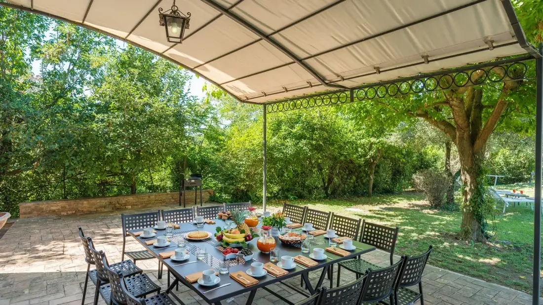 Una zona de comedor al aire libre está bajo un toldo junto a un jardín frondoso.