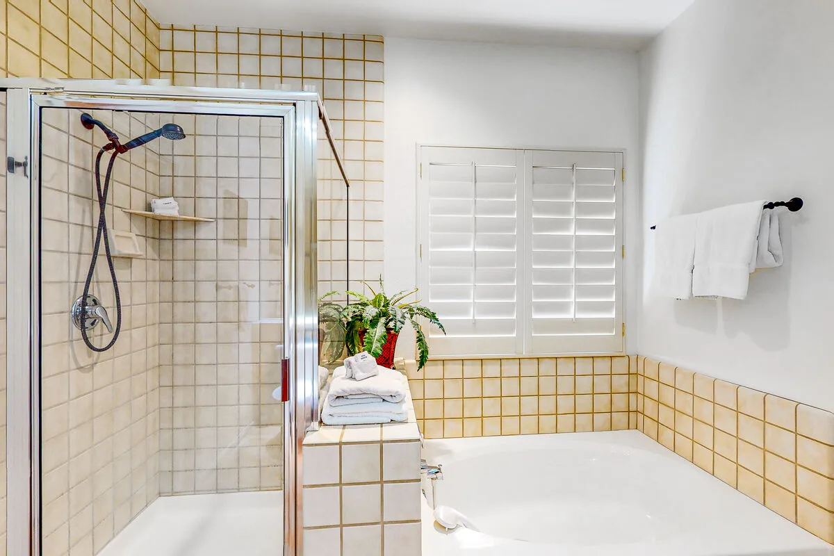 Un baño con ducha de vidrio, bañera y contraventanas.