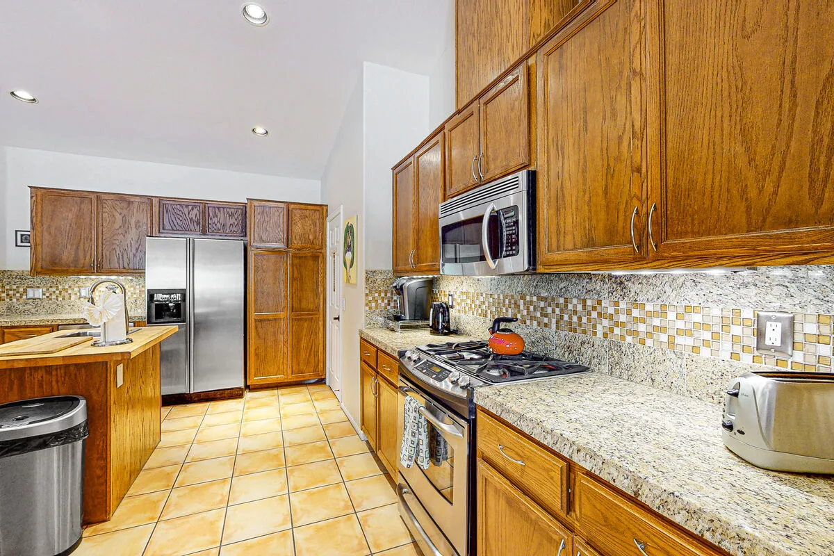 Una cocina con gabinetes de madera, un salpicadero de azulejos y electrodomésticos de acero inoxidable.