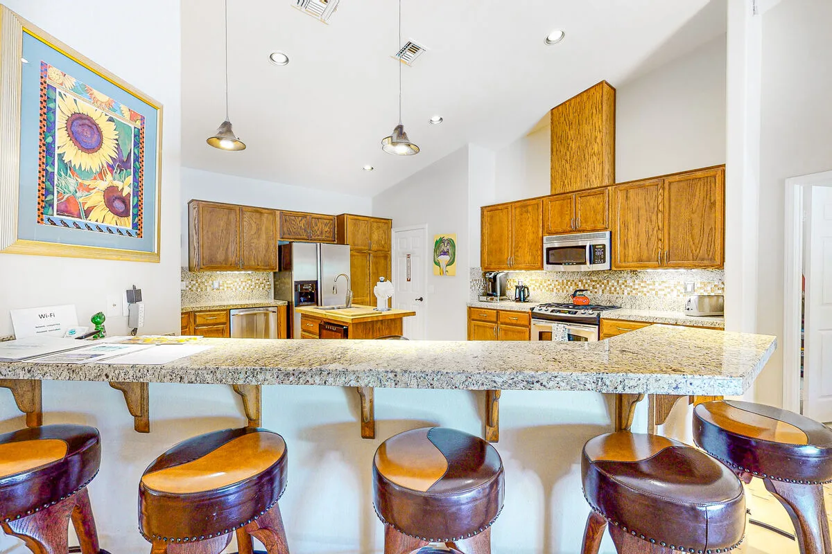 Una cocina luminosa con gabinetes de madera y una barra de granito con asientos.