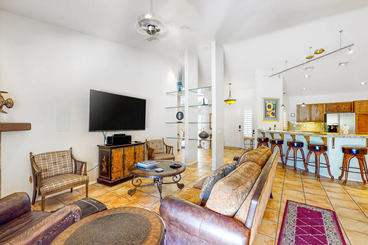 Una sala luminosa se abre a una barra de cocina, con asientos y un televisor.