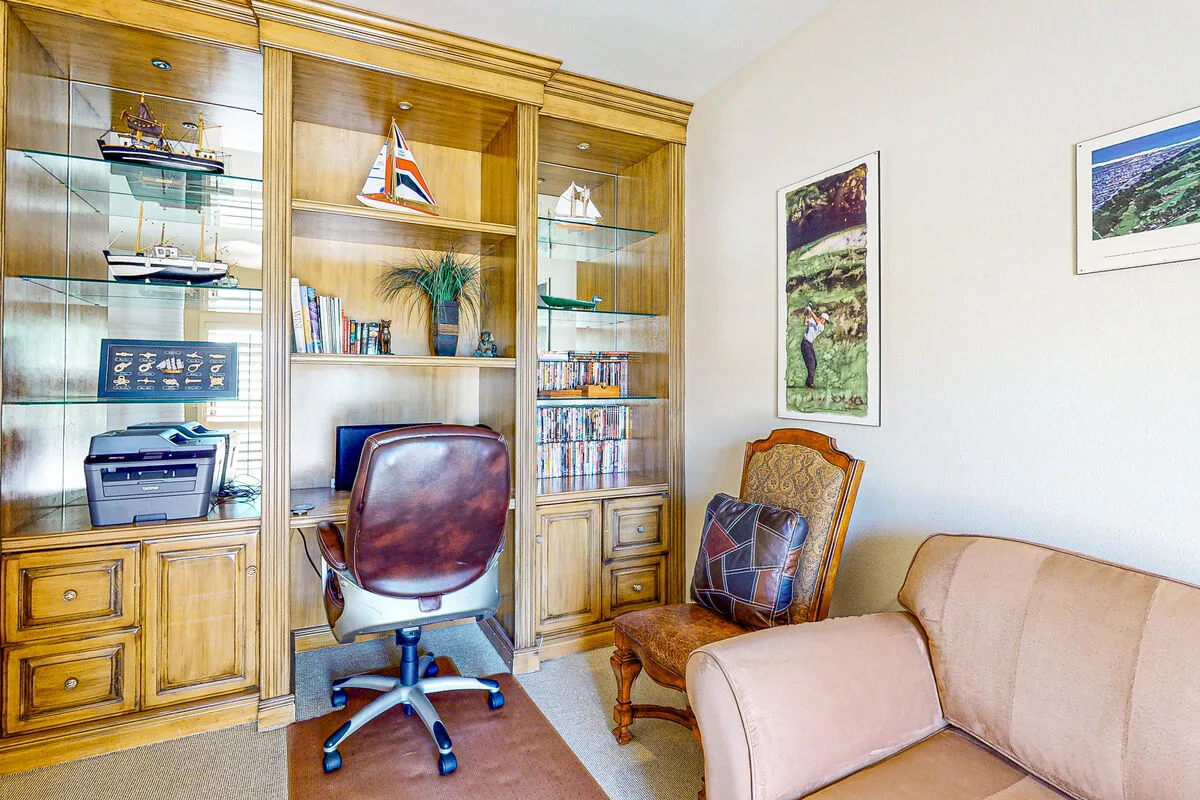 Un estudio con estanterías de madera, una silla de escritorio y un sofá.
