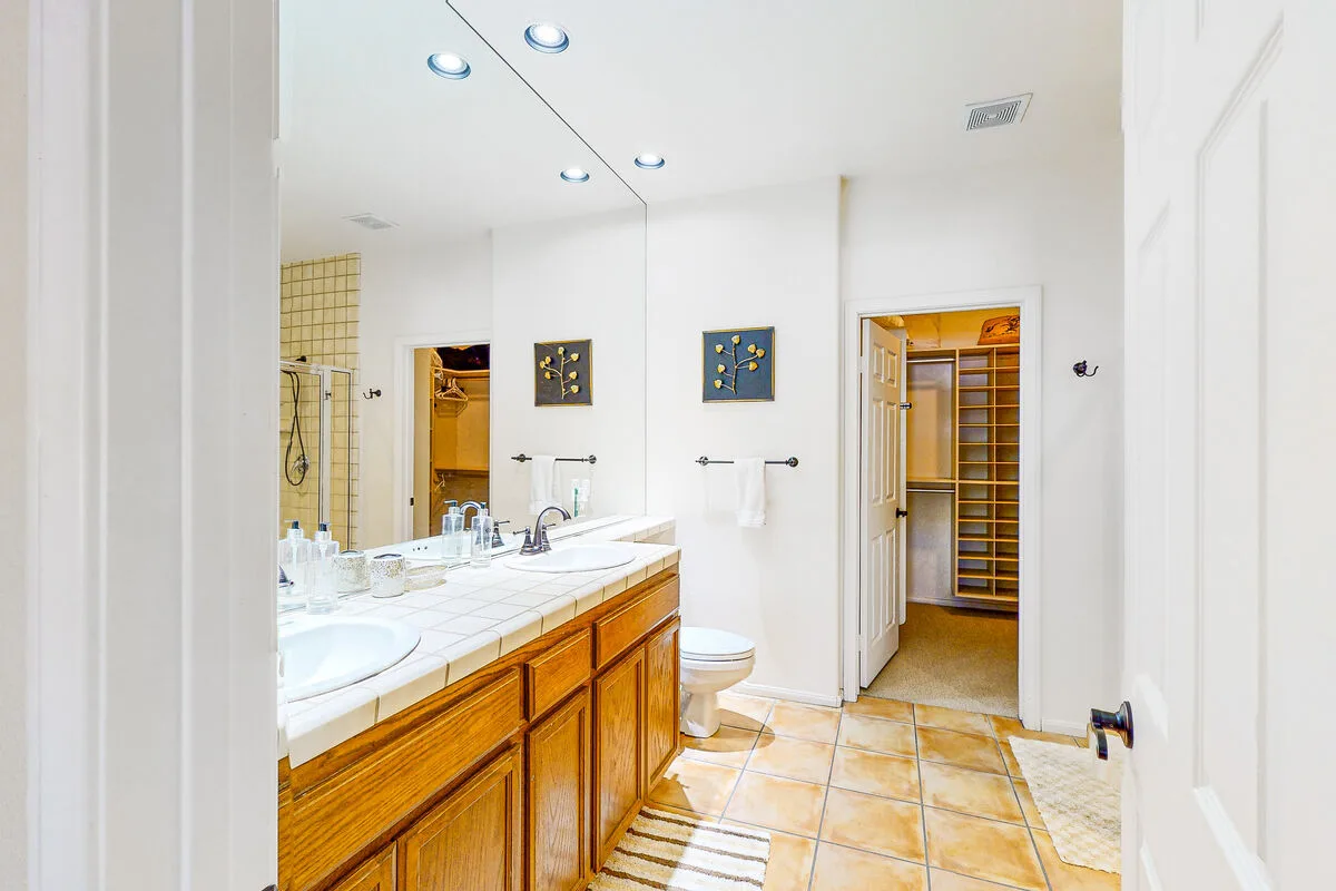 Un baño luminoso tiene un tocador largo, un espejo y una puerta abierta.
