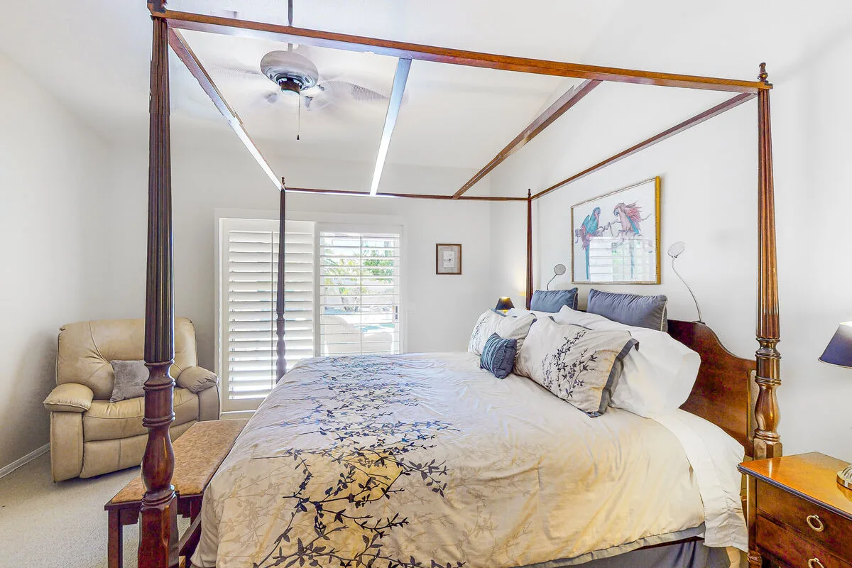 Un dormitorio con una cama con dosel grande y una ventana con persianas blancas.