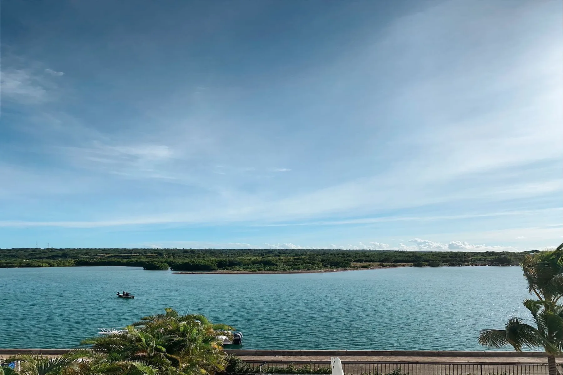A waterfront view shows calm blue water, a distant green shoreline, and open sky.