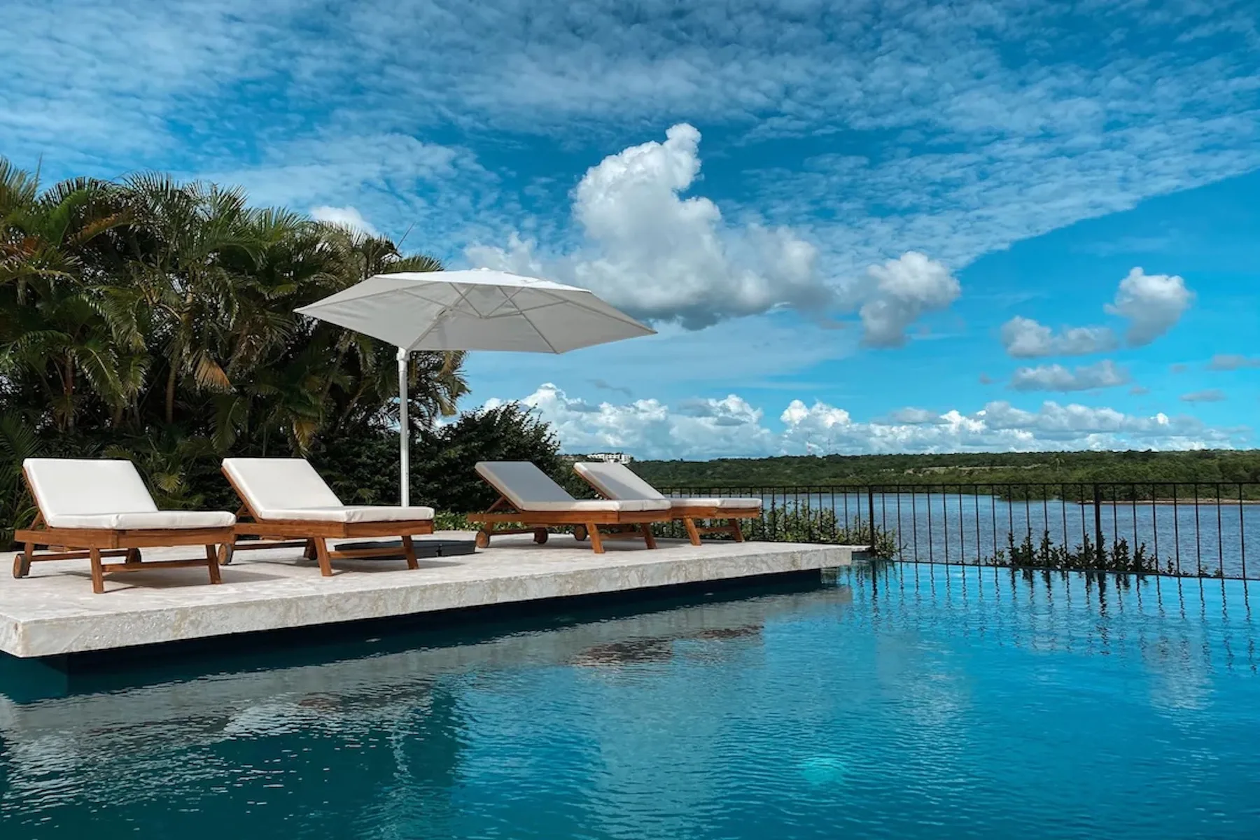 An outdoor poolside seating area with loungers and a large umbrella overlooks the water.