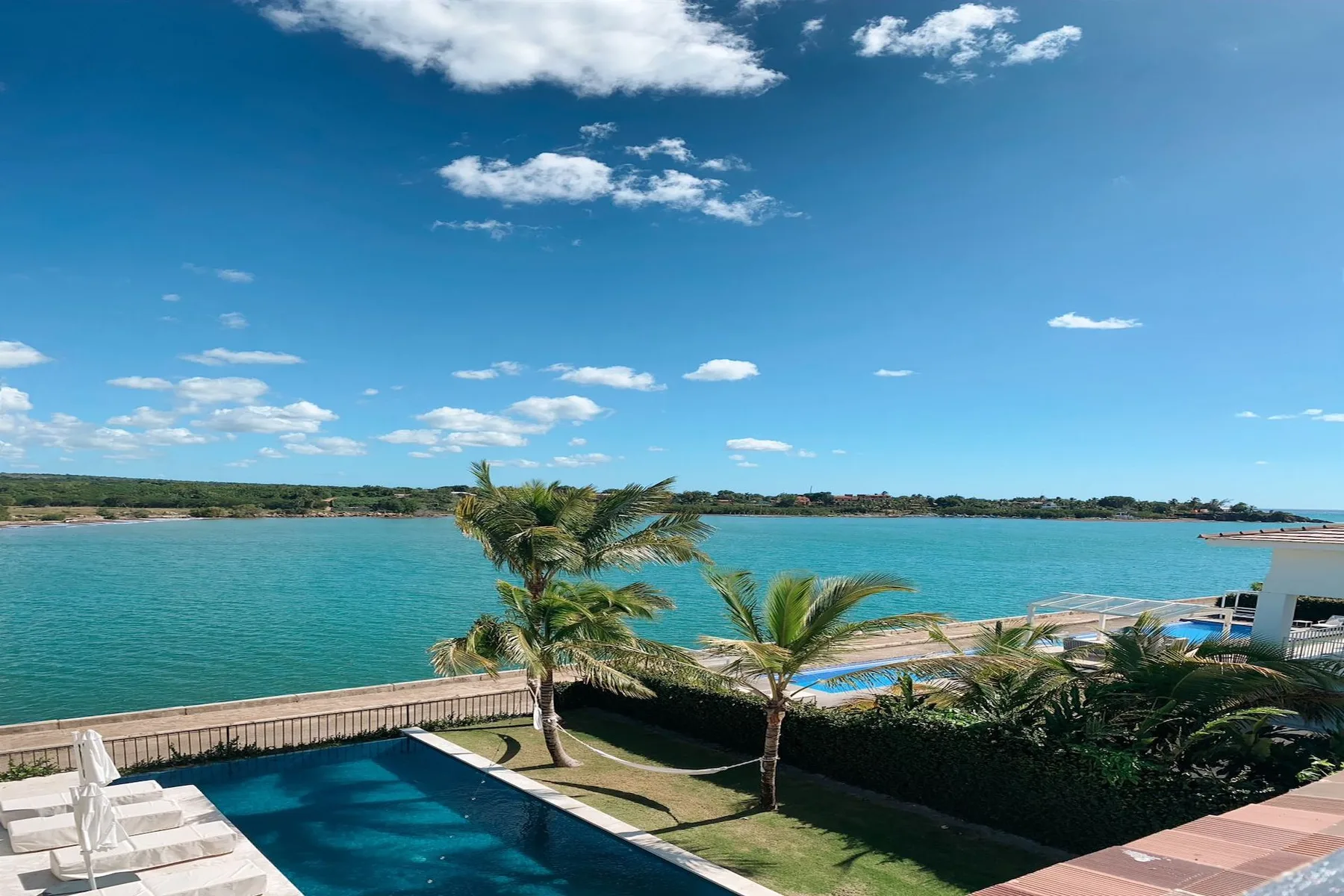 An outdoor pool overlooks a turquoise body of water beneath a bright blue sky.