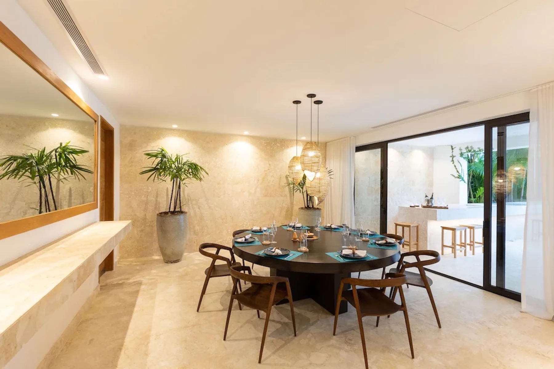 A dining area features a round table beneath hanging lights, with glass doors opening to a patio.