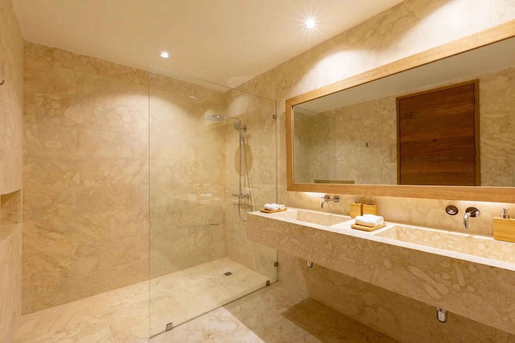 A marble-tiled bathroom with a walk-in shower and a wide mirror above the sink.
