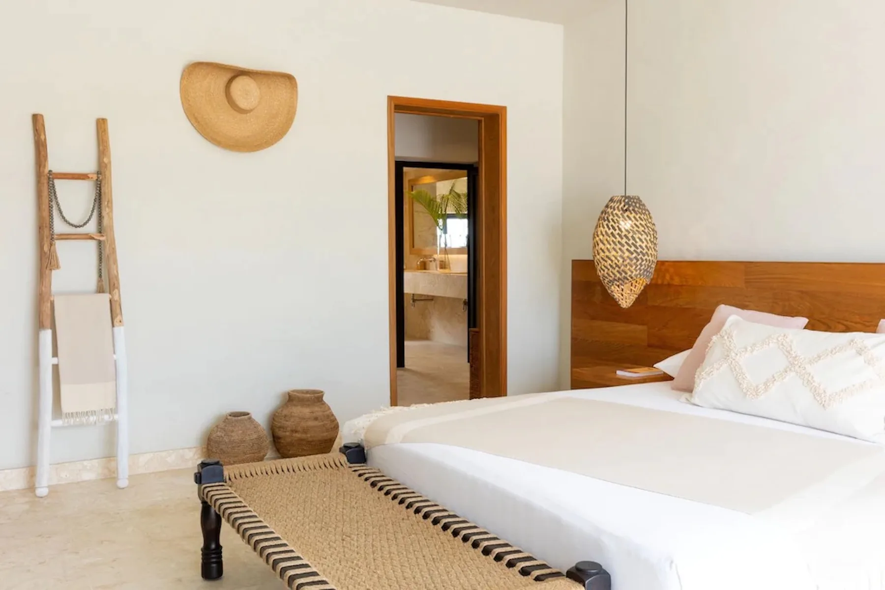 A bedroom with a white bed, woven bench, and natural wall decorations.