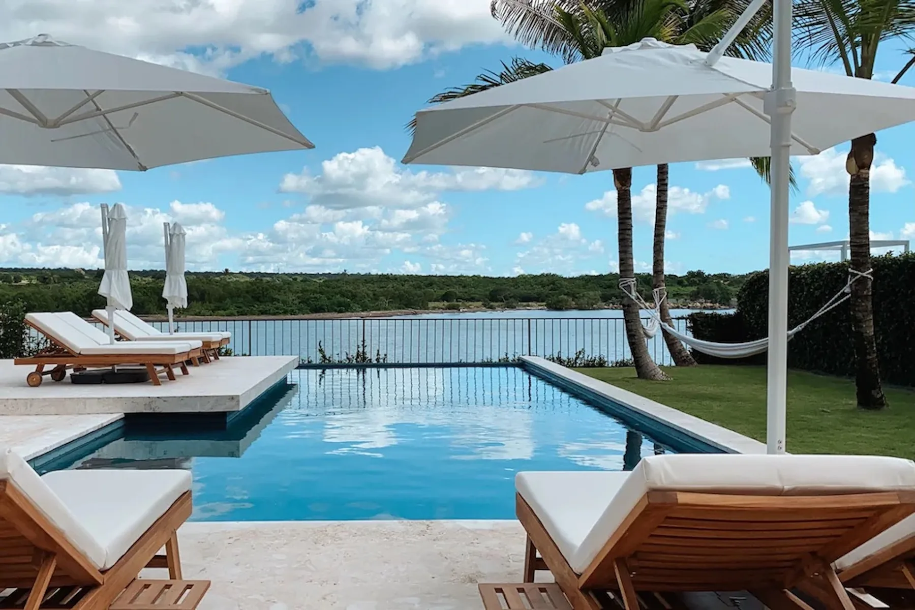 An outdoor pool overlooks a body of water, with loungers and umbrellas nearby.