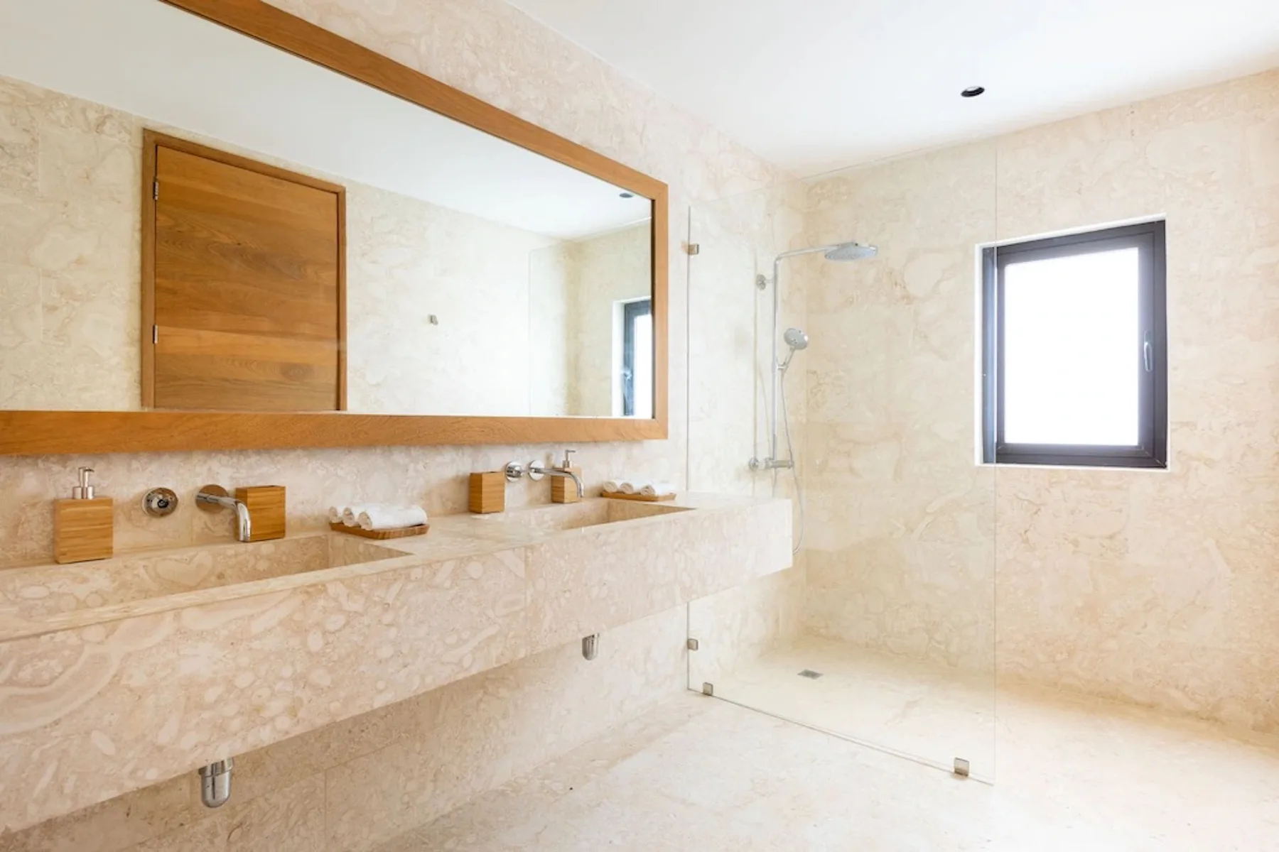 A bright bathroom with a long mirror, sink counter, and glass shower.