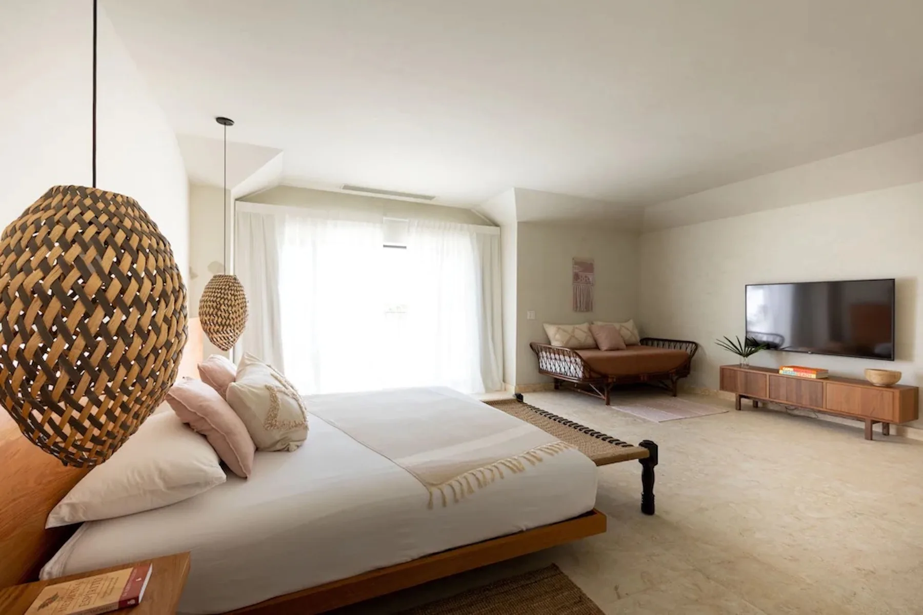 A bright bedroom with a bed, woven pendant lights, and a television.