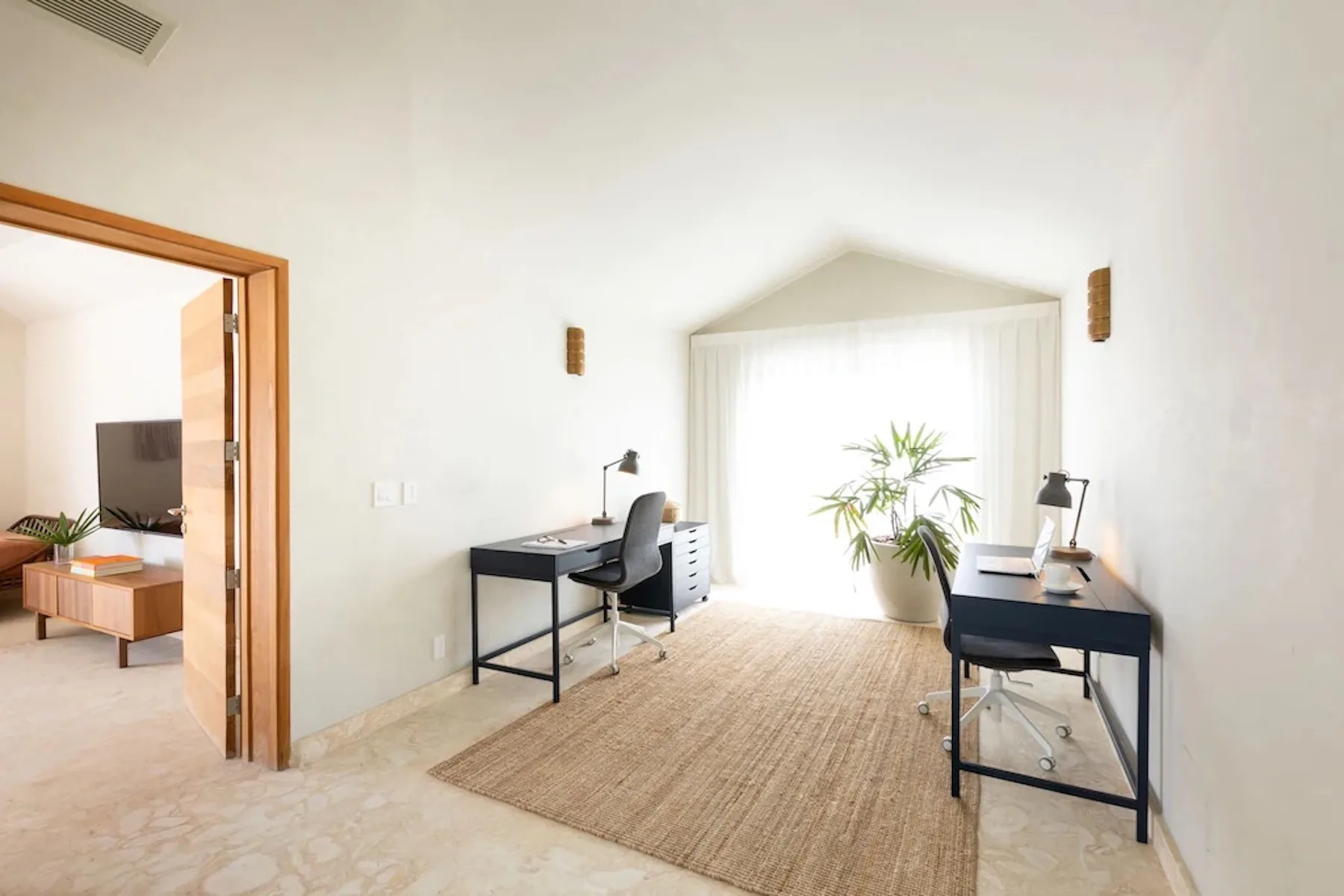 A bright workspace with two desks, a rug, and a large window.