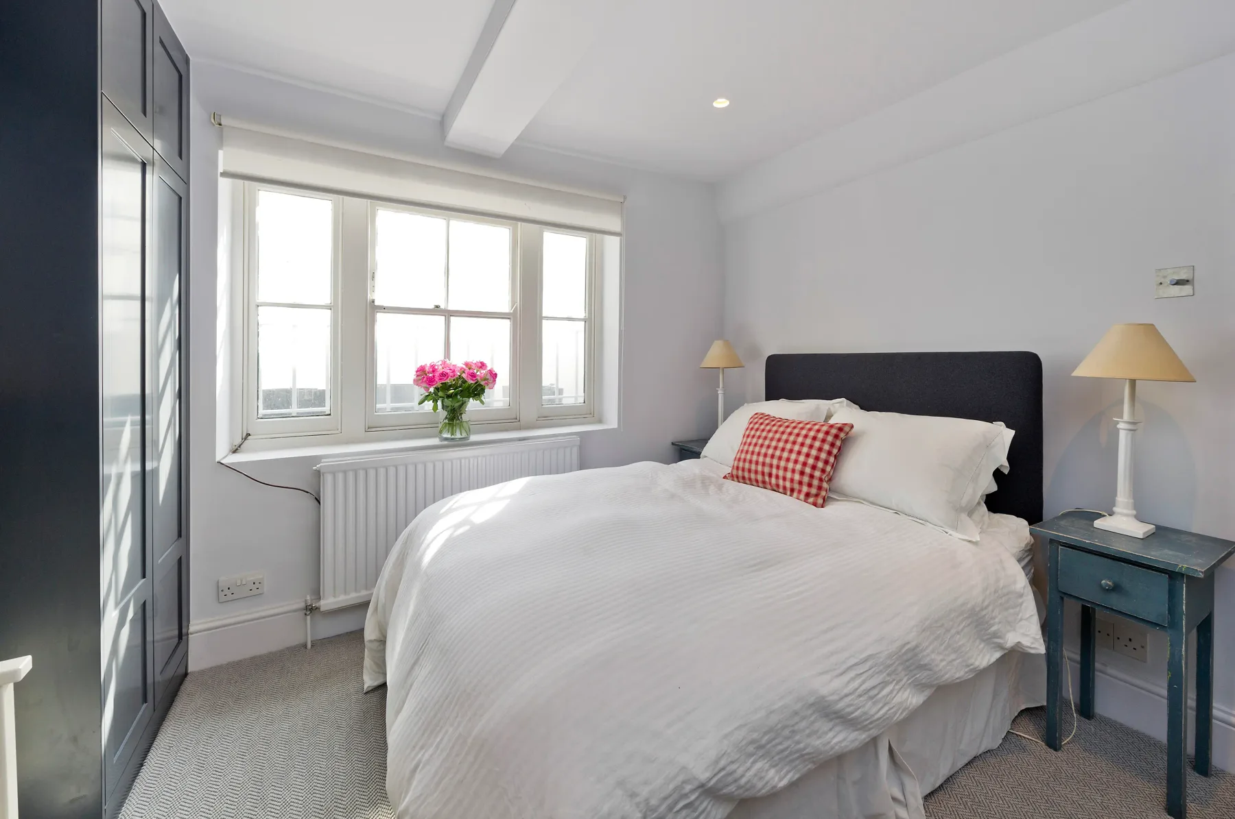 Un dormitorio luminoso con una cama tendida junto a grandes ventanas.