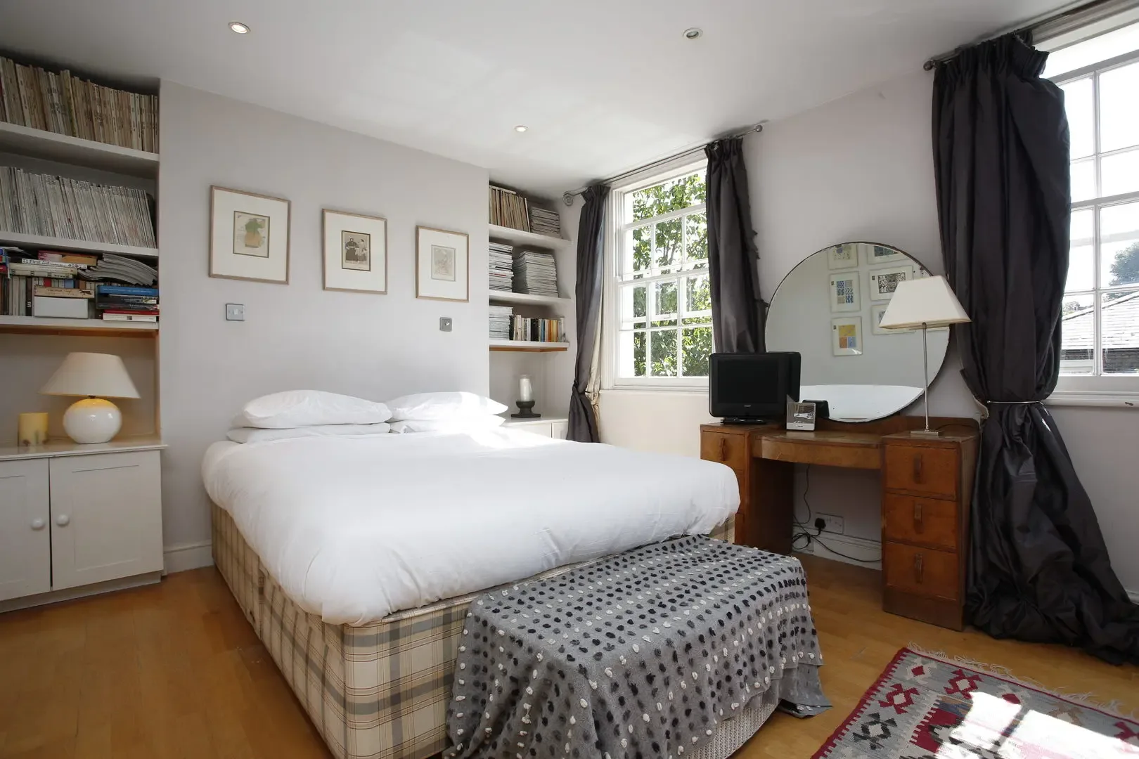 Un dormitorio luminoso con una cama blanca, estantes empotrados y un escritorio de madera.