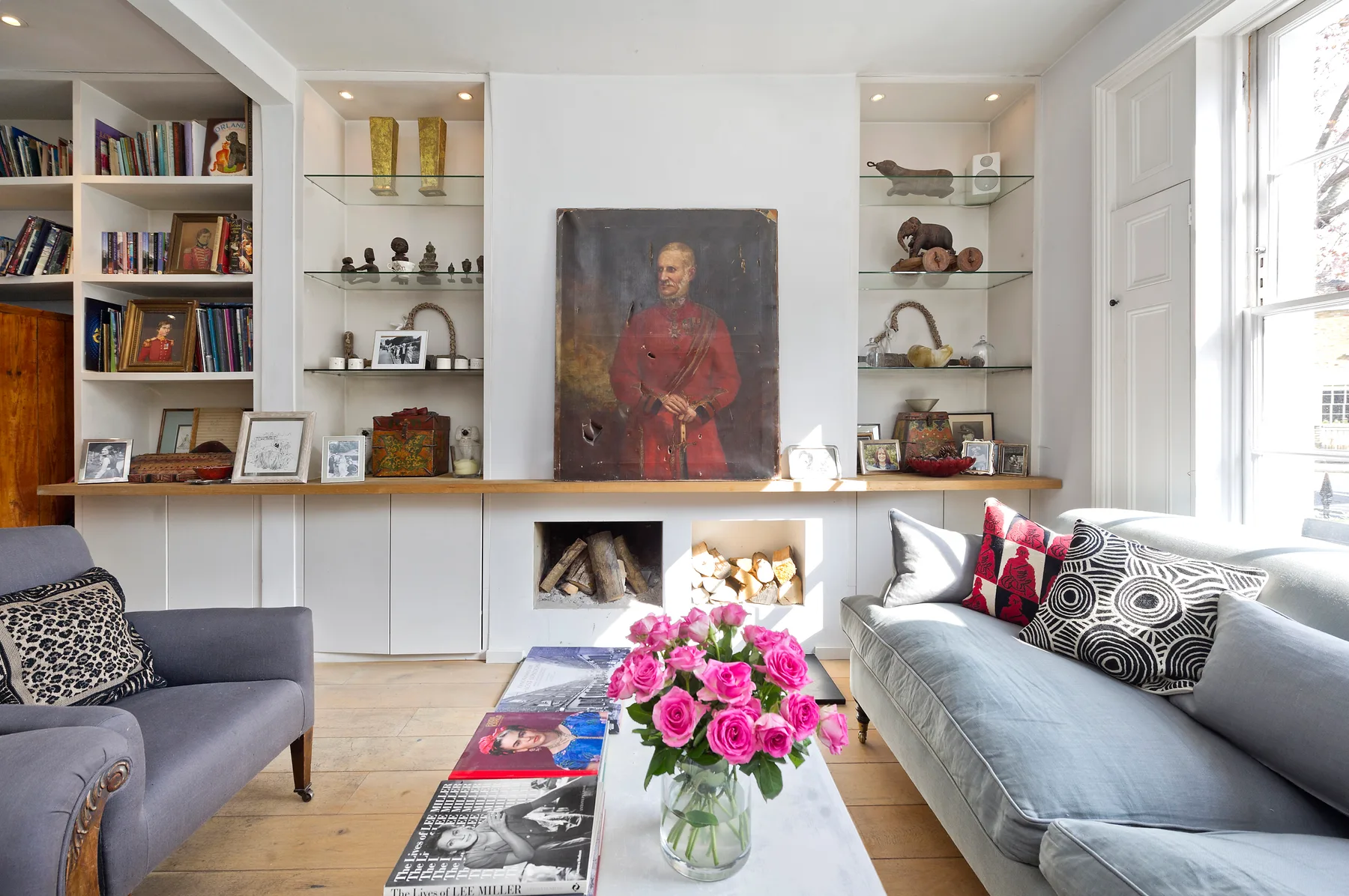 Una sala luminosa con asientos, estanterías empotradas y un arreglo de flores.