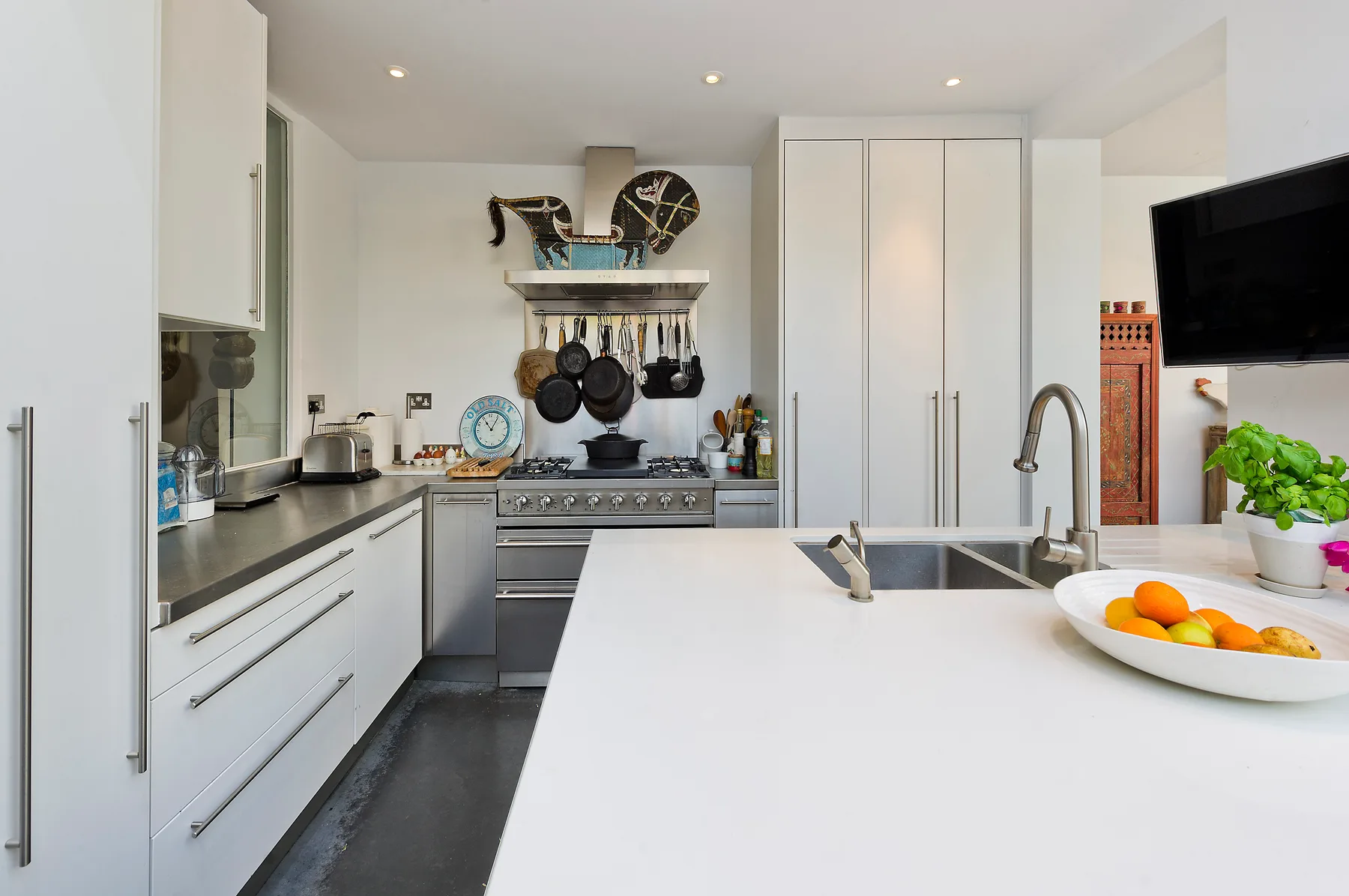 Una cocina moderna y luminosa con armarios blancos, una isla central y sartenes sobre la estufa.