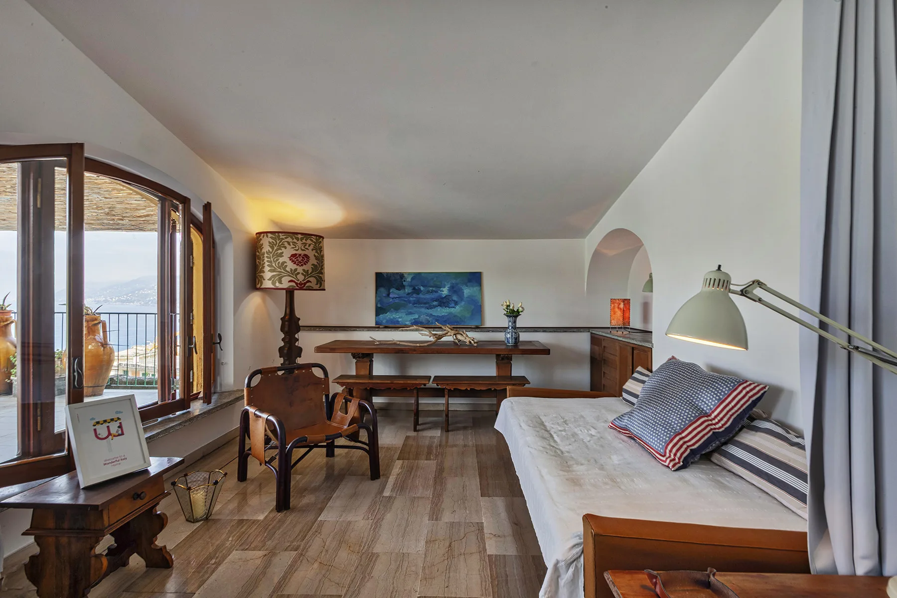 Una habitación amueblada con cama, escritorio y ventanas con vistas a un balcón.