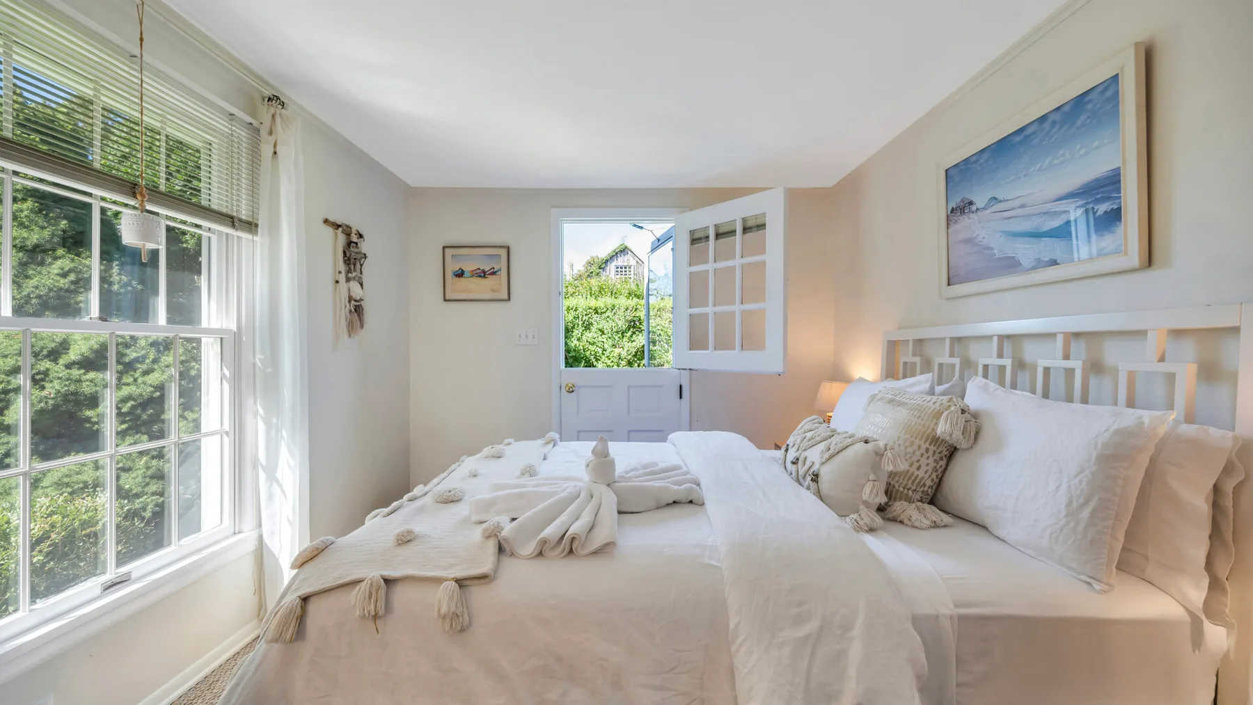 Un dormitorio luminoso con ropa de cama blanca y grandes ventanas frente a la vegetación.