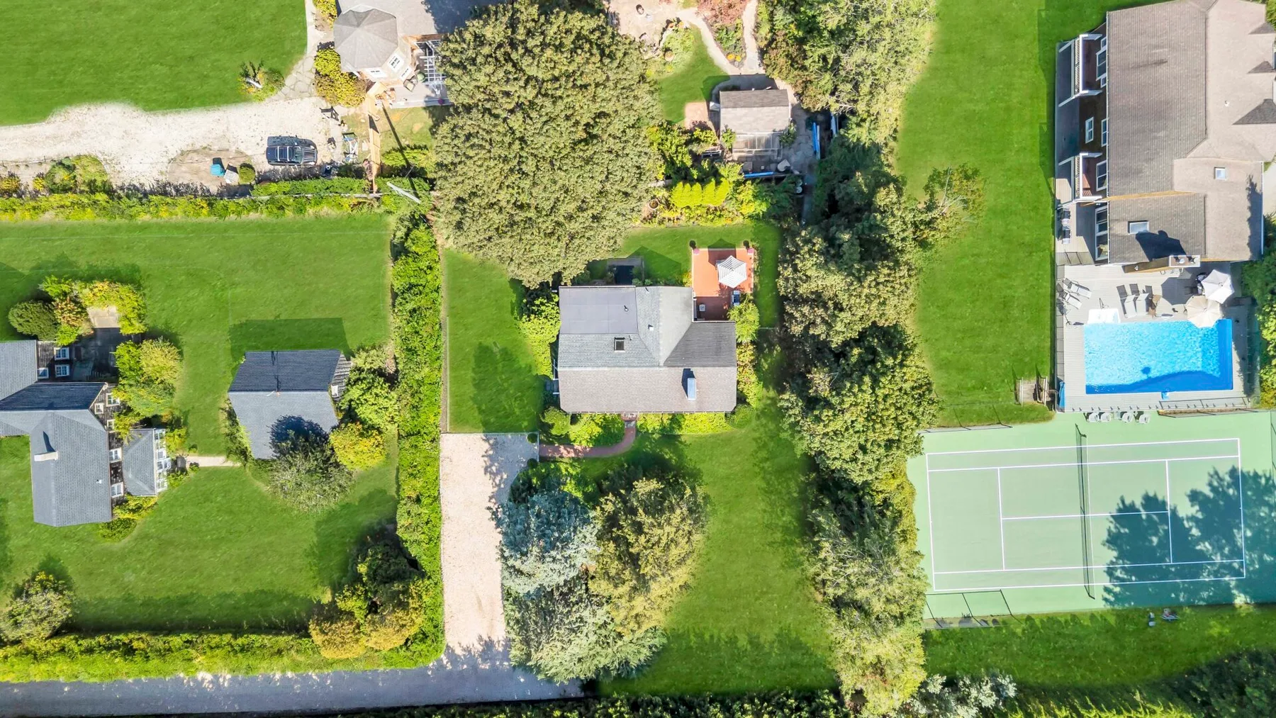 Una vista aérea muestra casas, céspedes y una piscina junto a una cancha de tenis.