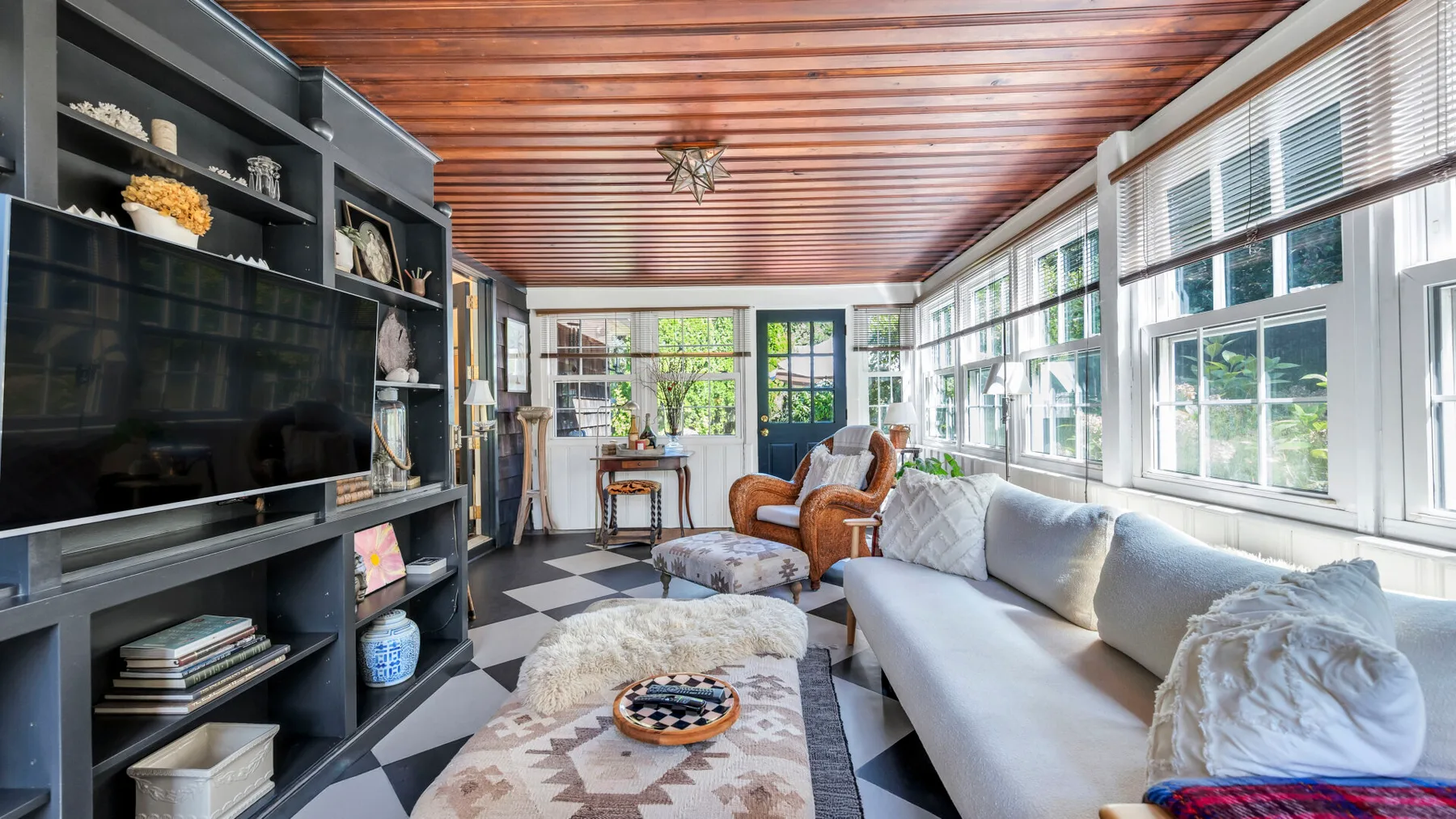 Una sala luminosa con grandes ventanas, un sofá largo y estanterías empotradas.