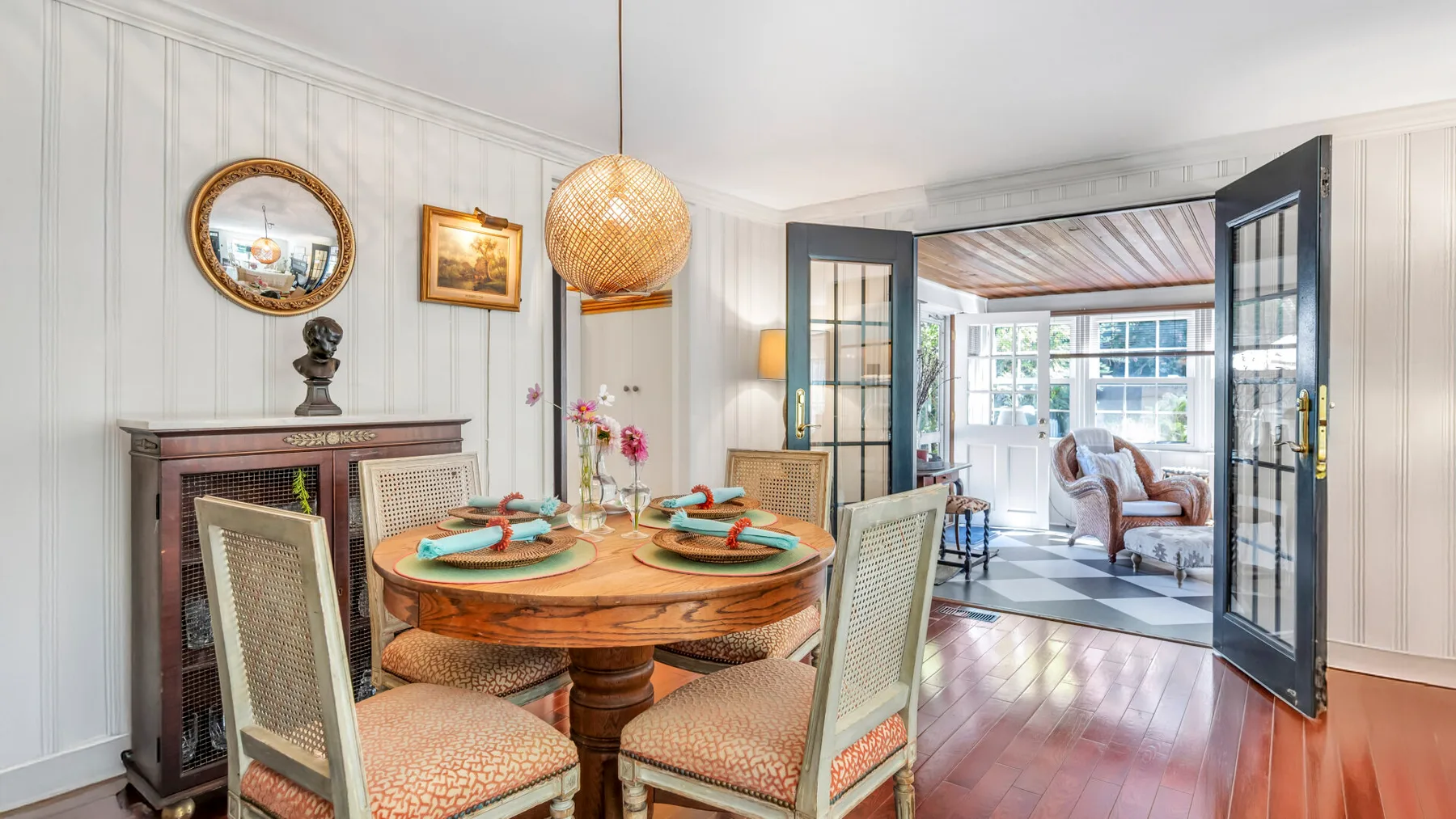 Comedor con una mesa redonda de madera y puertas abiertas hacia una sala de estar.