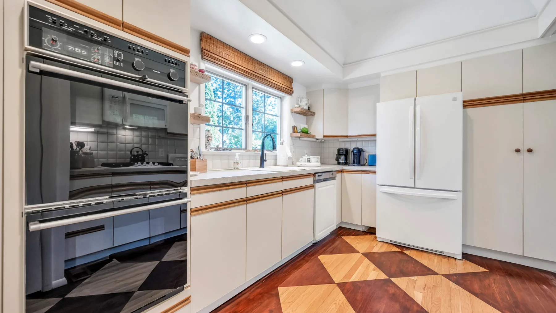 Una cocina luminosa con hornos empotrados, gabinetes blancos y una ventana sobre la encimera.