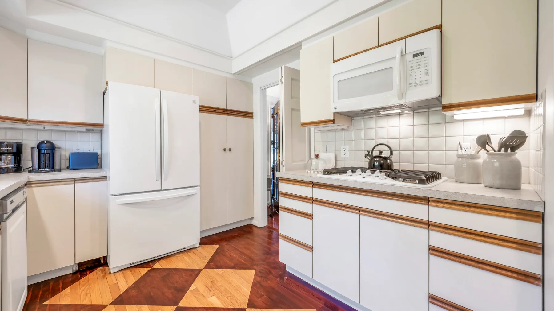 Una cocina luminosa con gabinetes blancos, refrigerador y salpicadero de azulejos.
