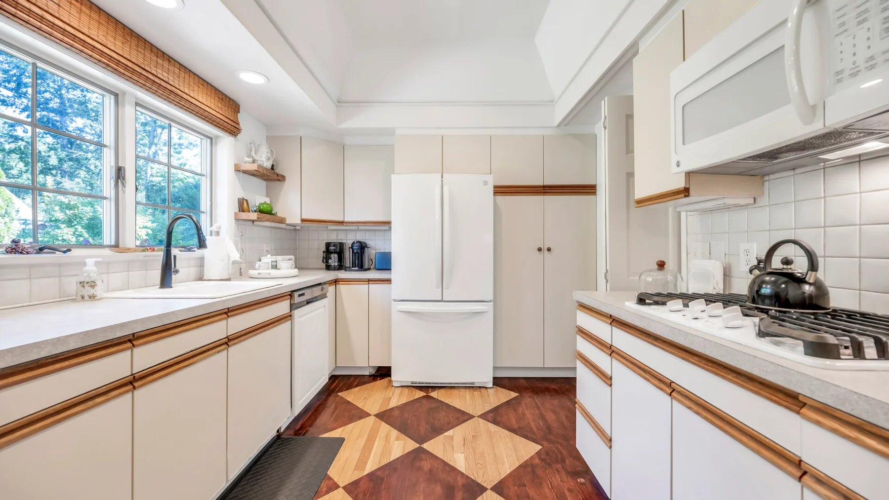 Una cocina luminosa con gabinetes blancos, encimeras largas y un piso estampado.