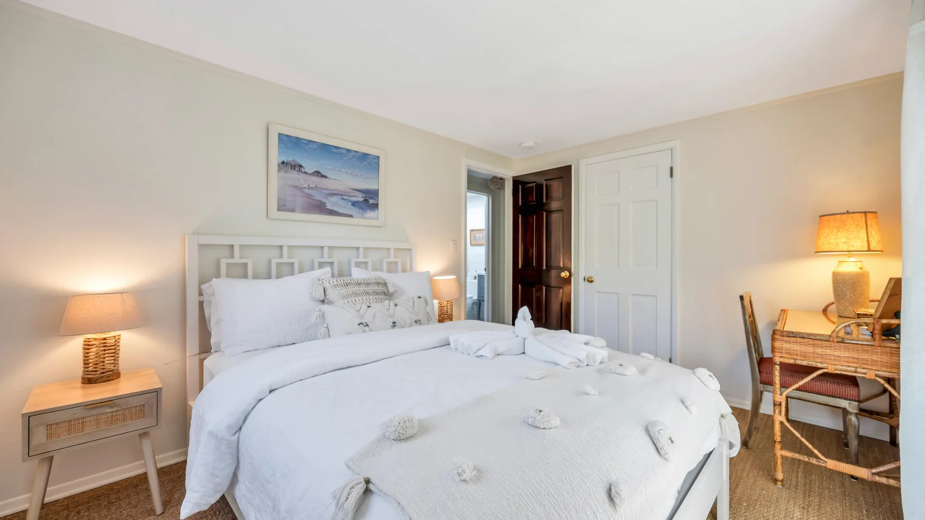Un dormitorio luminoso con una cama blanca y un cuadro sobre el cabecero.