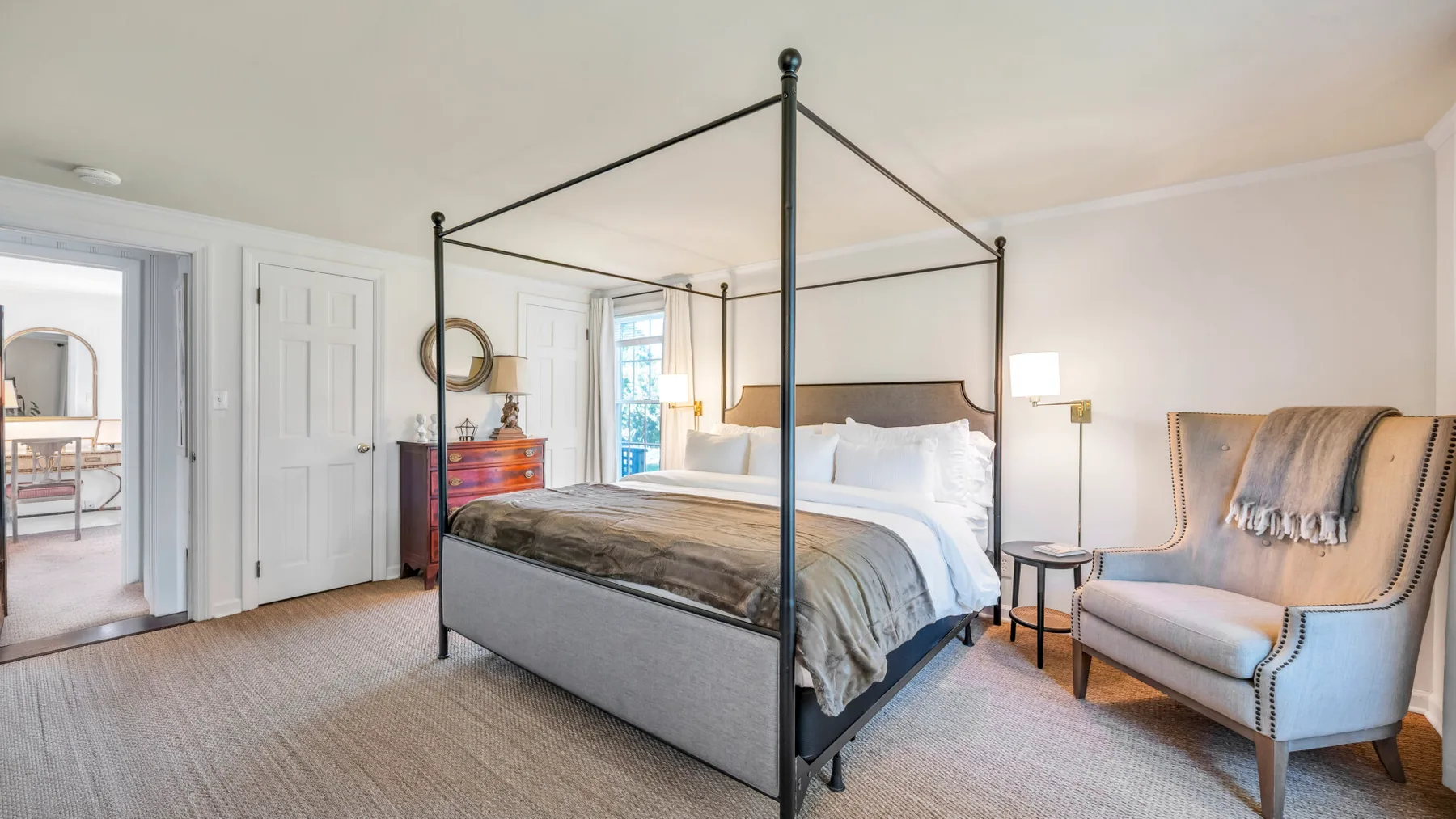 Un dormitorio luminoso con una cama con dosel y un sillón tapizado.