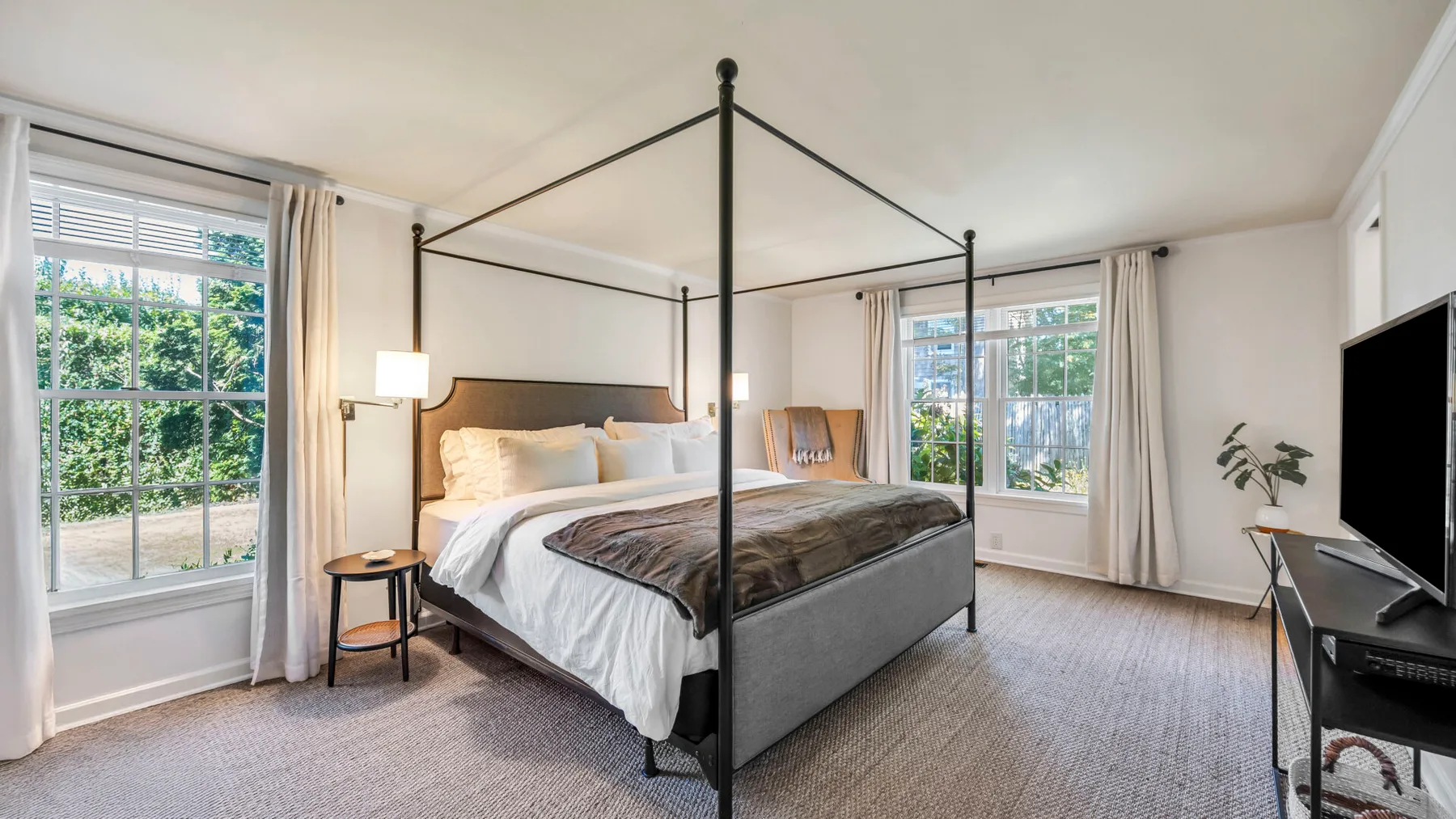 Un dormitorio luminoso cuenta con una cama con dosel y grandes ventanas.
