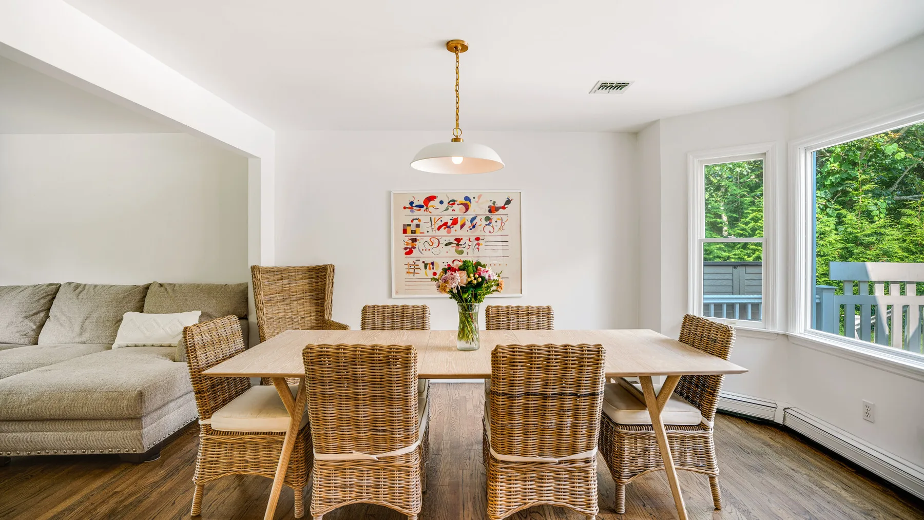 A bright dining area with a wooden table and wicker seating beside large windows.