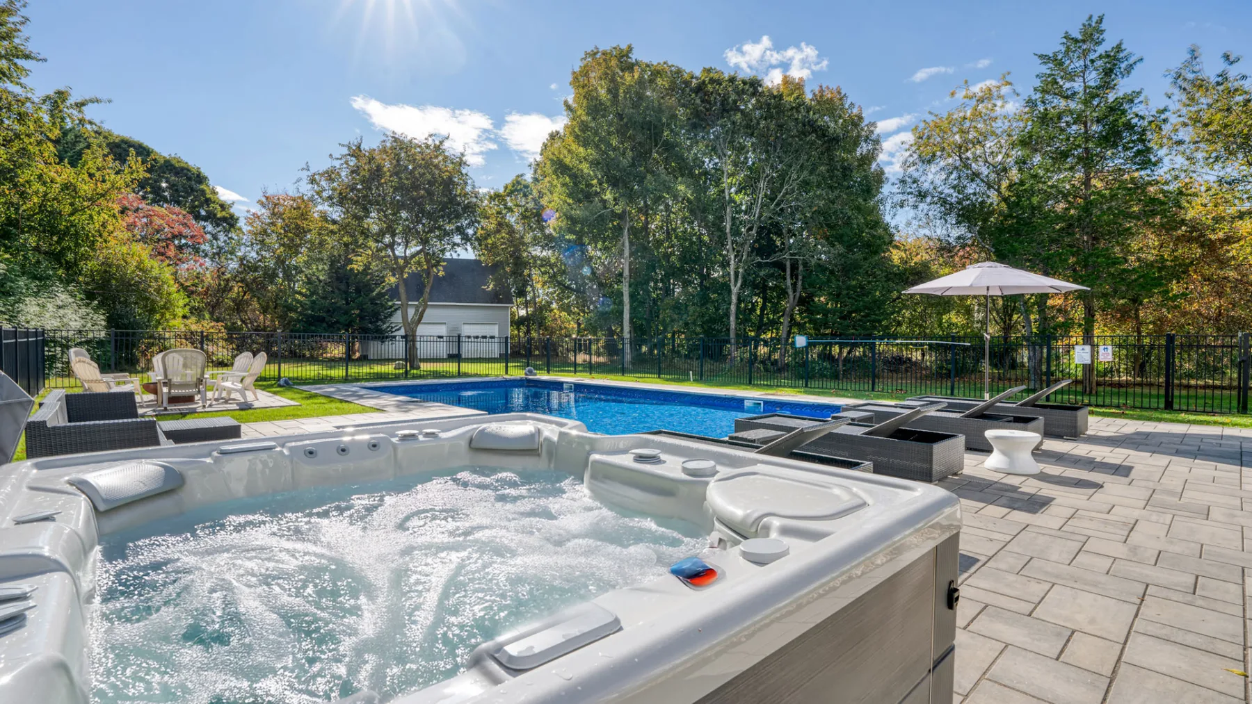 An outdoor pool and bubbling hot tub sit beside a paved patio.