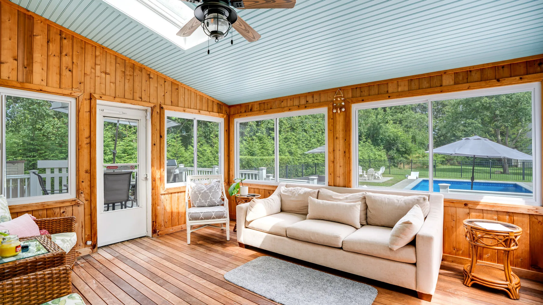 A sunroom with large windows overlooks a garden and swimming pool.