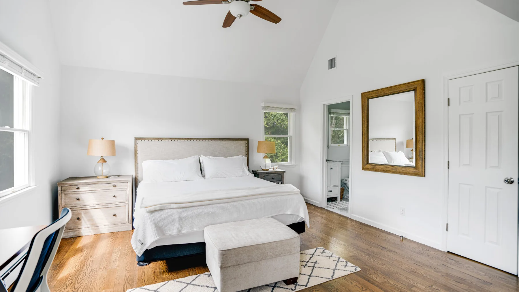 A bright bedroom with a bed, bedside tables, and a large window.