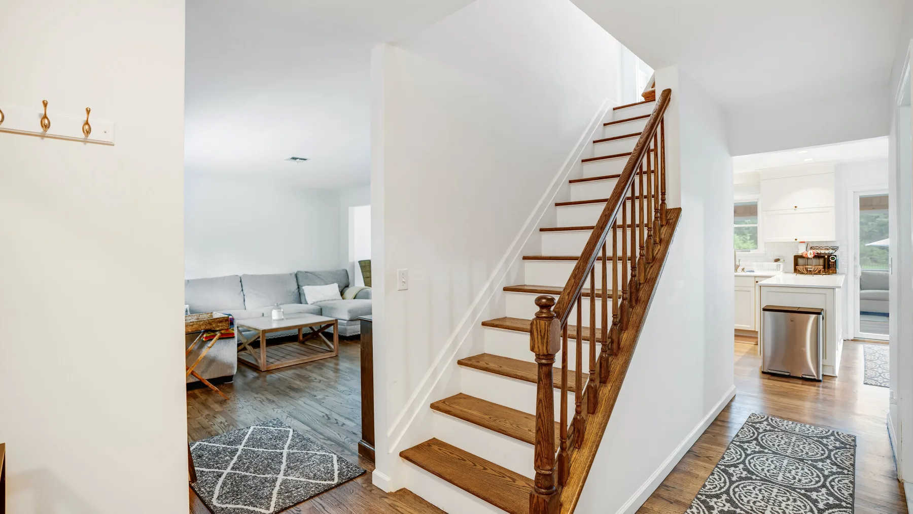 An interior hallway features a wooden staircase beside an open living area.