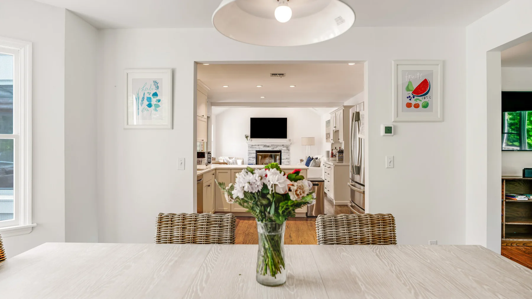 A bright dining area opens into a kitchen, with a flower arrangement on the table.