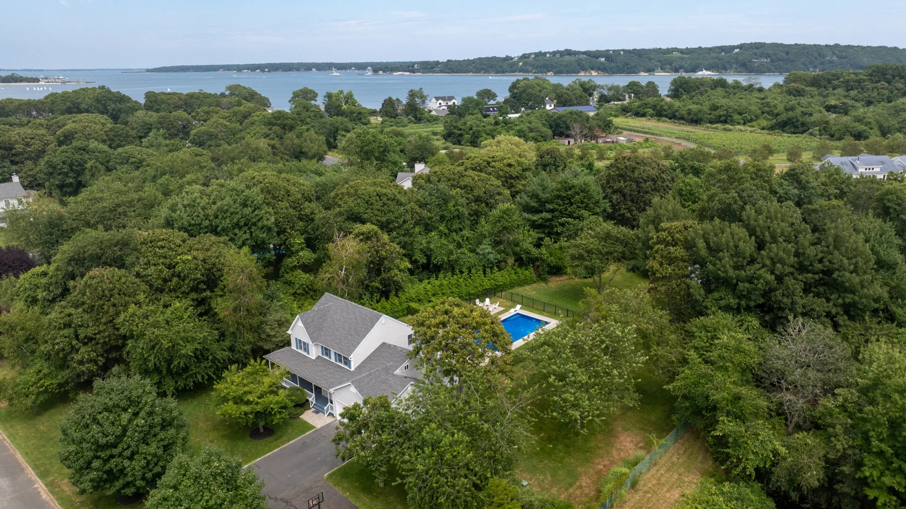 An aerial view of a house among trees, with water visible in the distance.