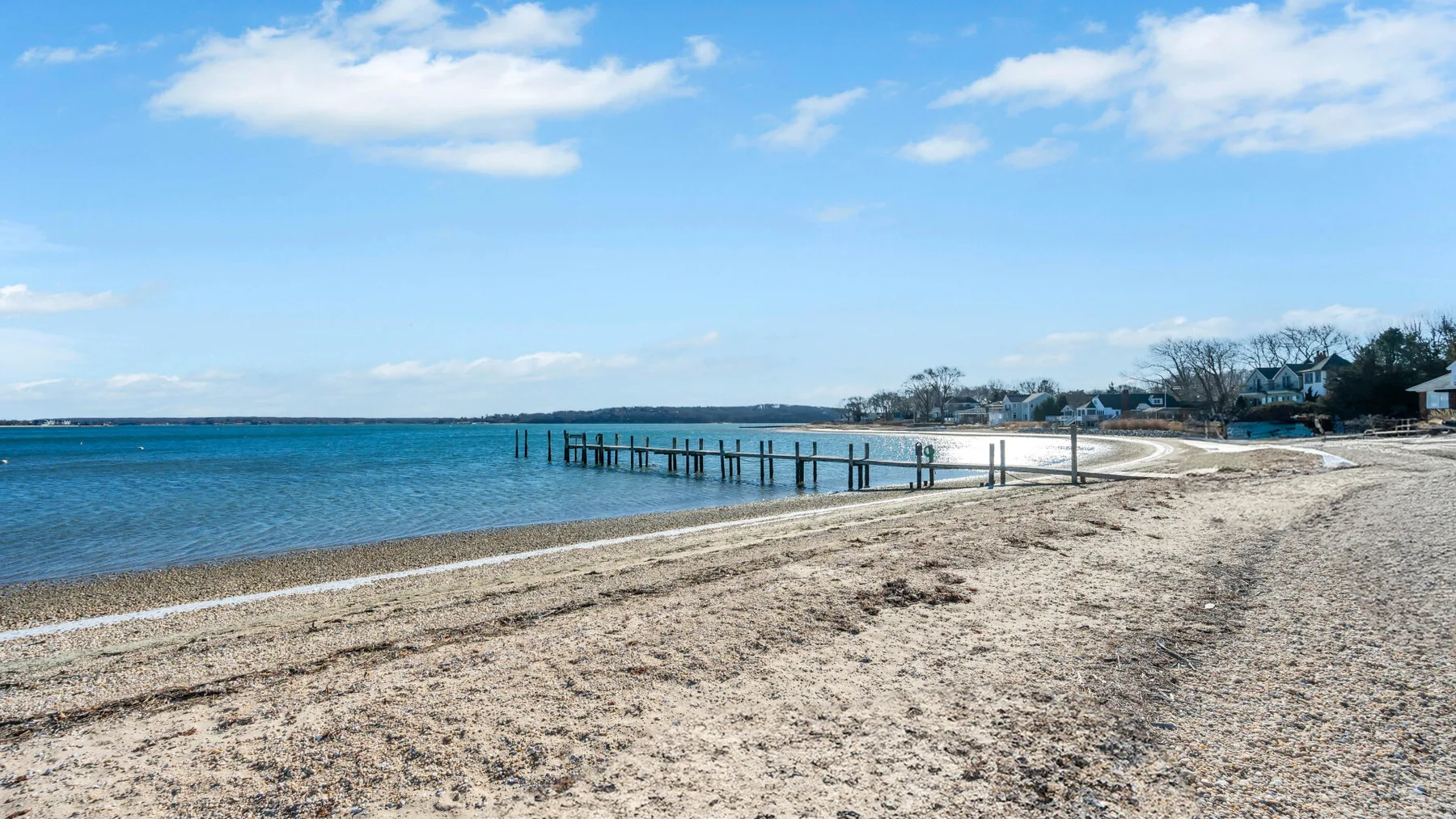 A sandy beach curves alongside calm blue water beneath a partly cloudy sky.