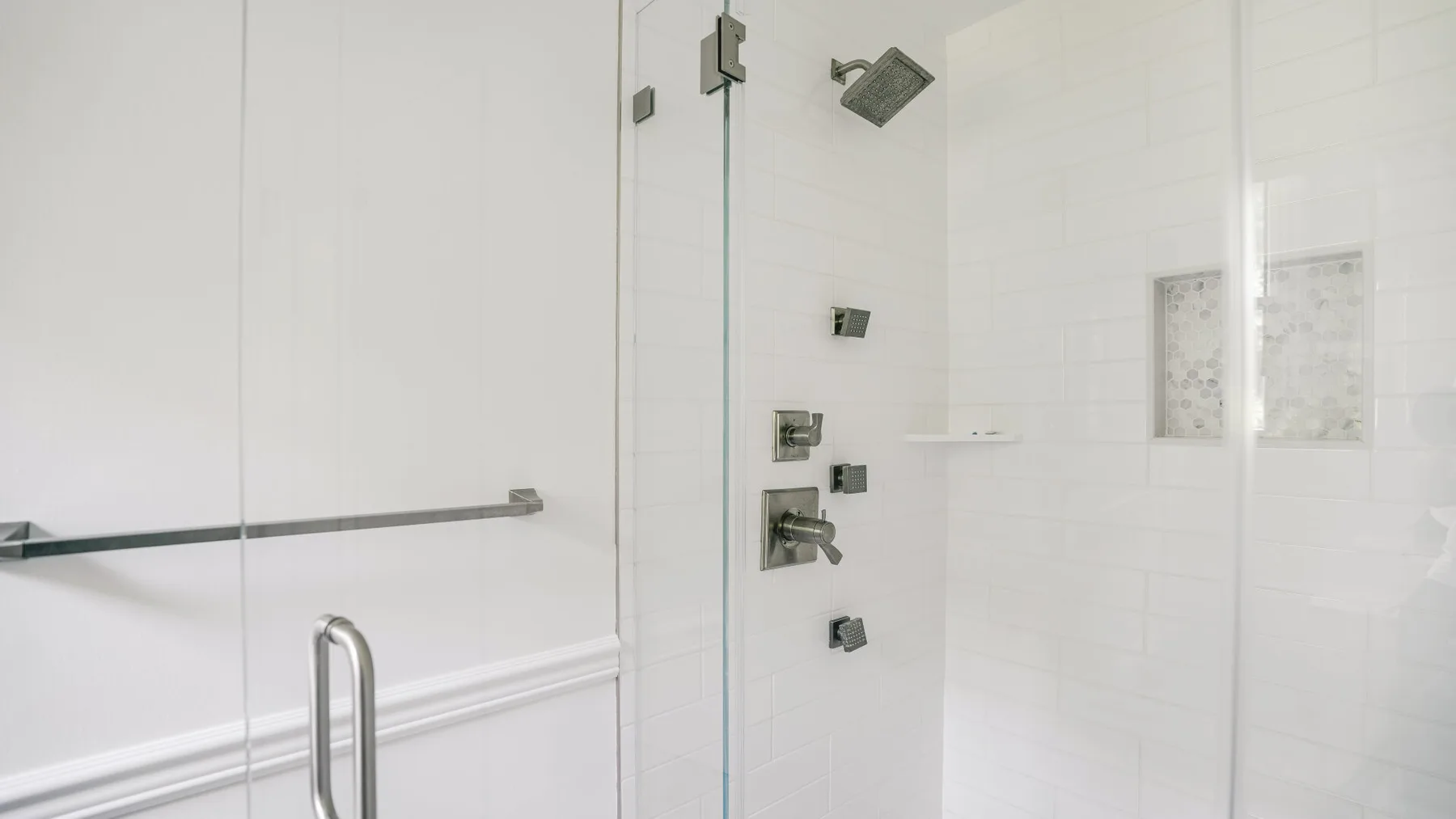 A bright tiled bathroom with a glass-enclosed shower and small window.