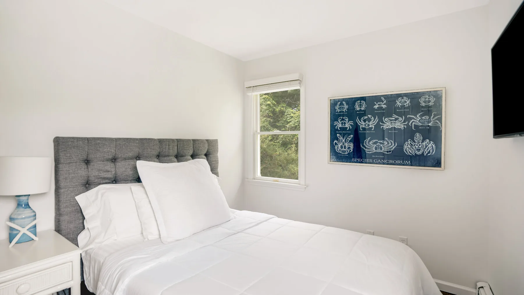 A bedroom with a neatly made bed, a window, and framed artwork.